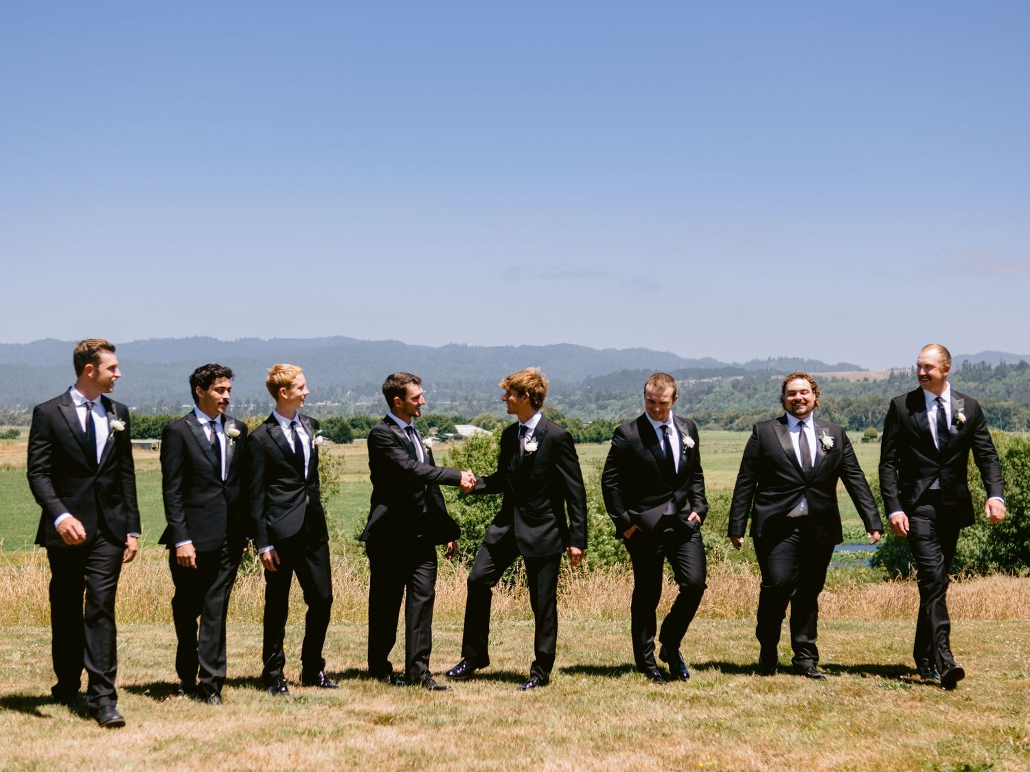 Groomsmen in black suits line up for a creative photo against a scenic mountain backdrop.