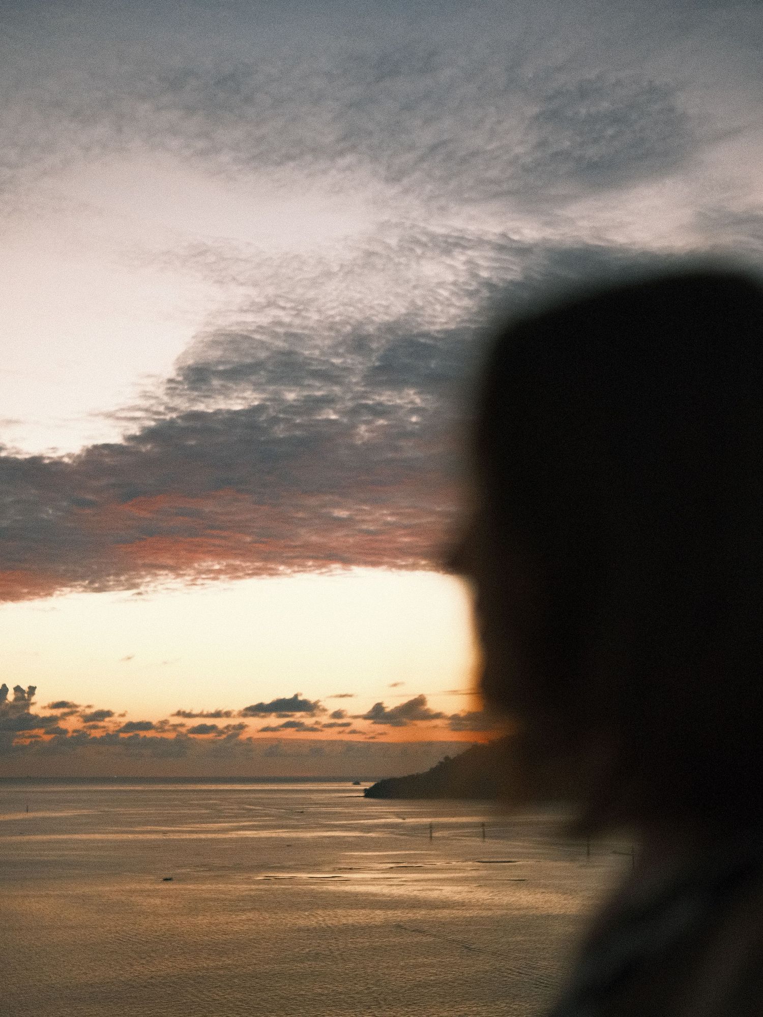 Dramatic sunset over ocean horizon with silhouetted cliffs and cloudy sky.