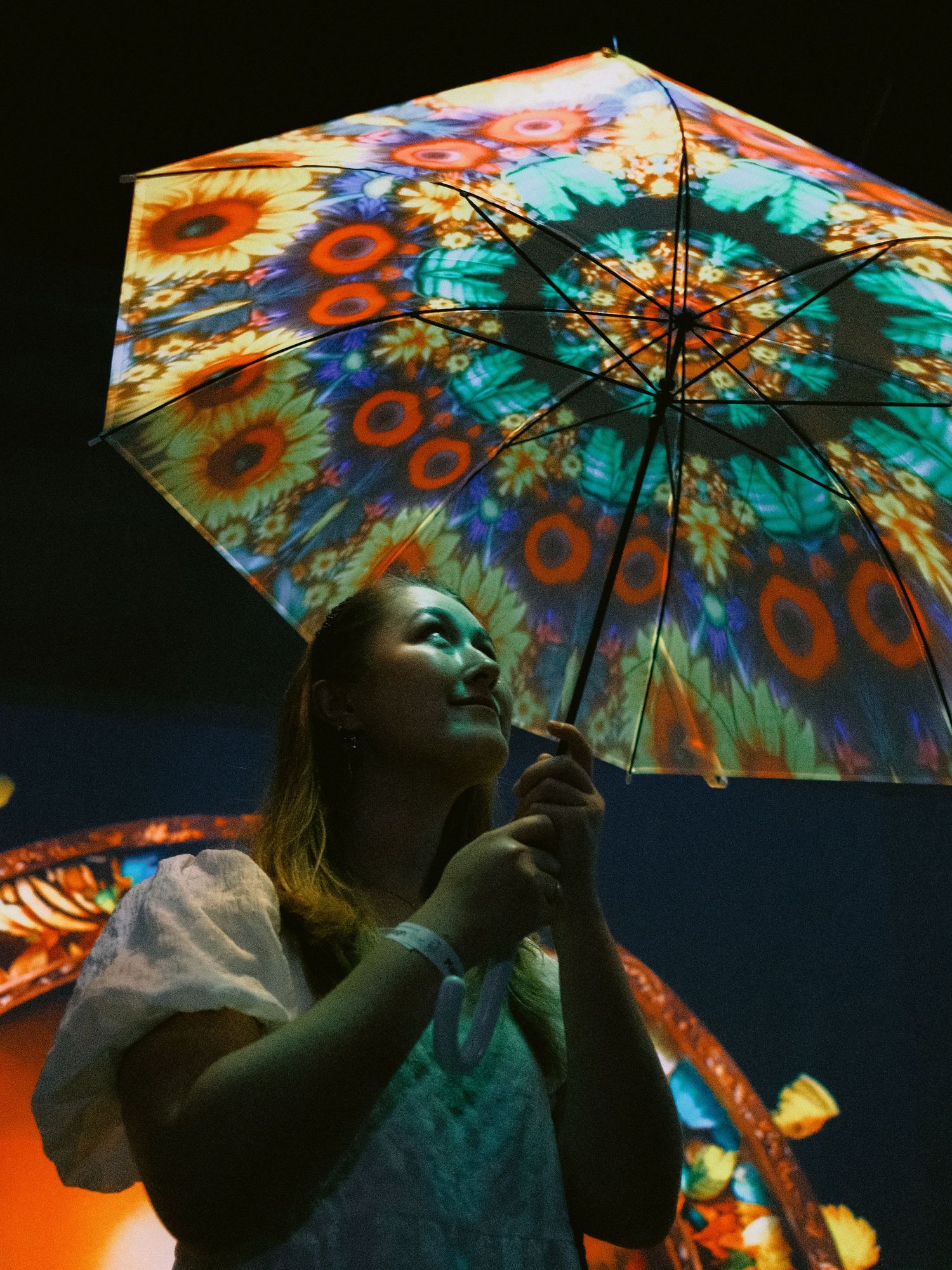 Colorful tie-dye patterned umbrella illuminated against a dark background.