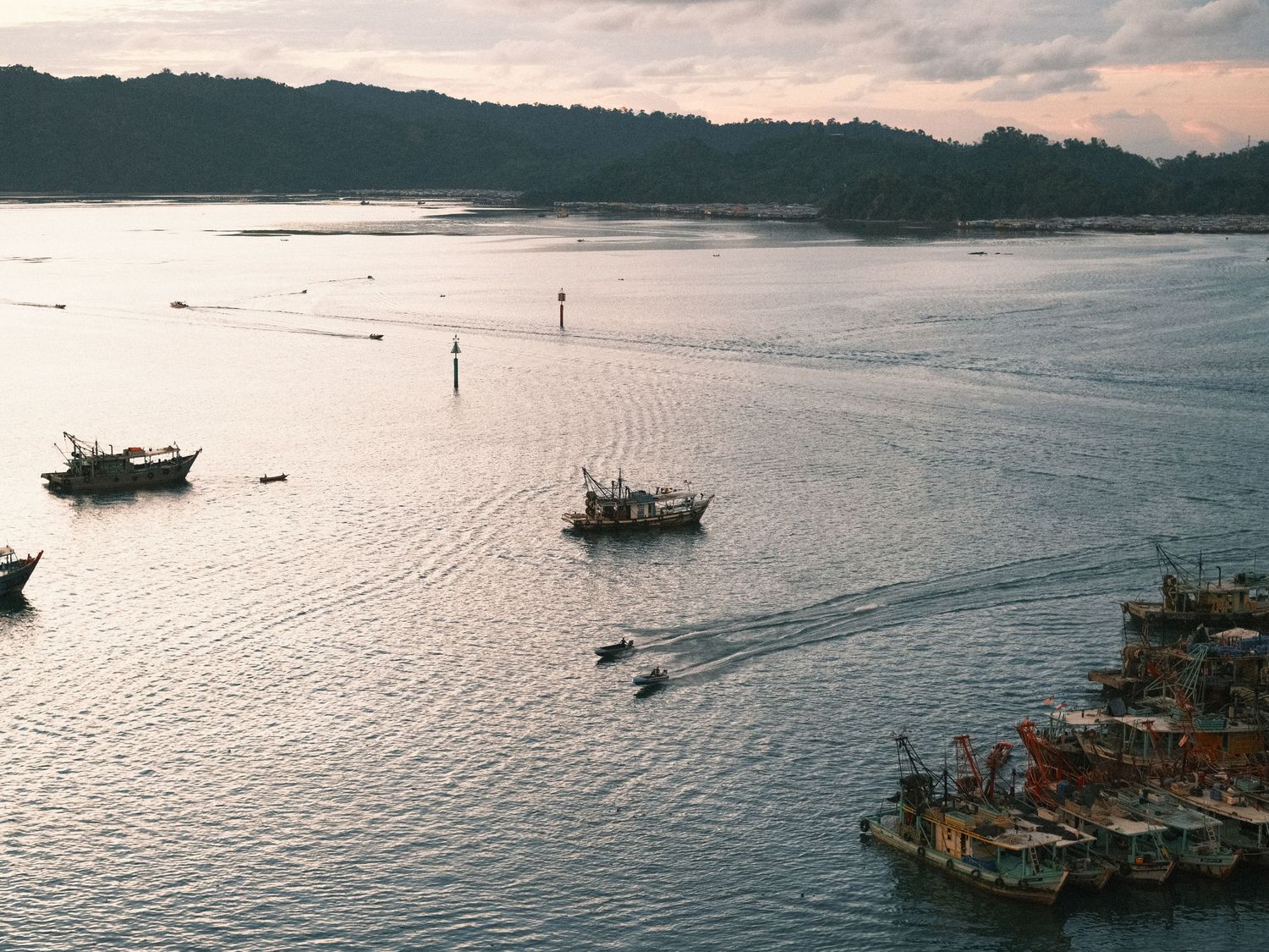 Panoramic view of boats on calm water during sunset with coastal landscape.