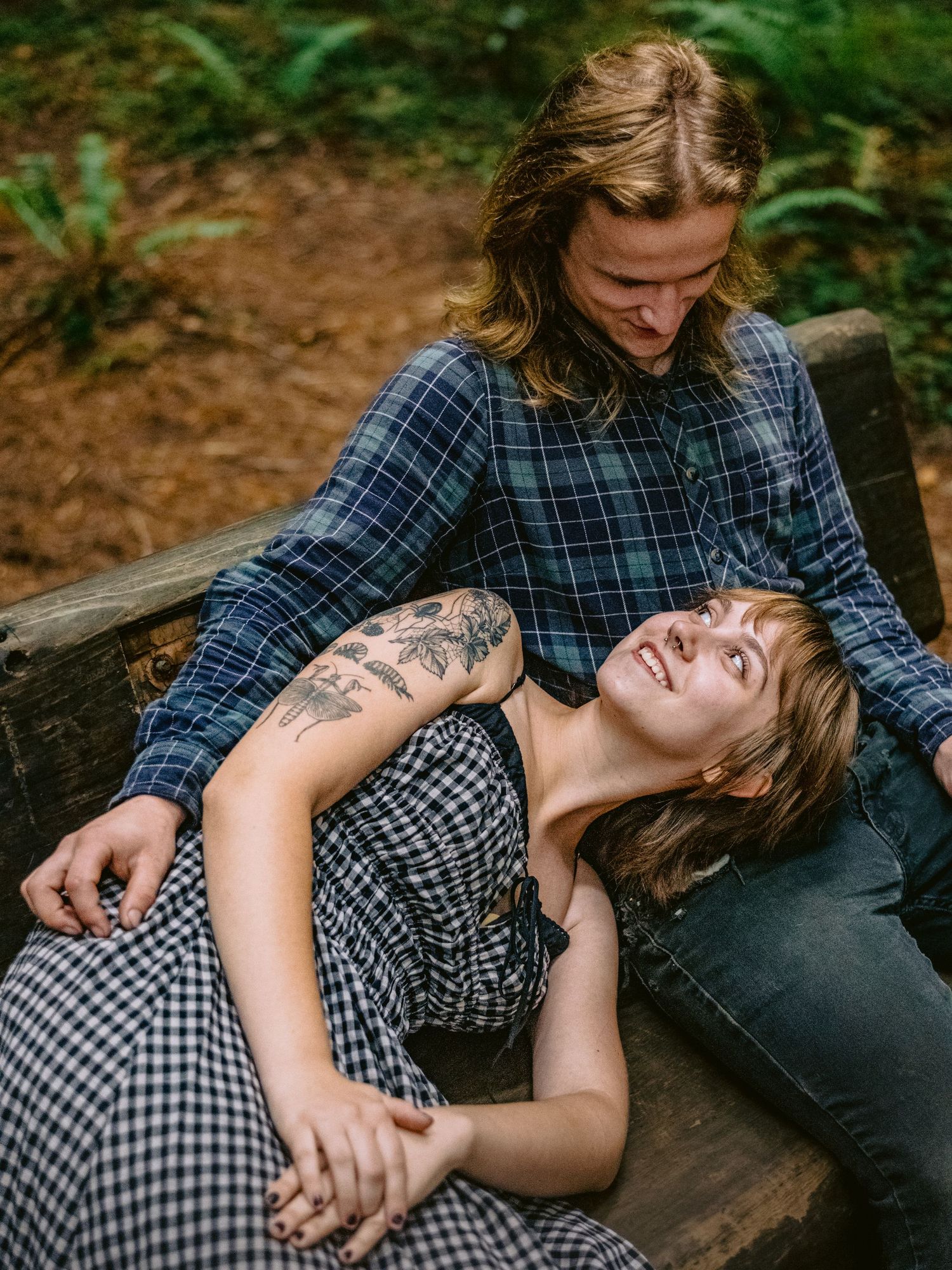 Couple in plaid and gingham relaxing on fallen log in forest setting.
