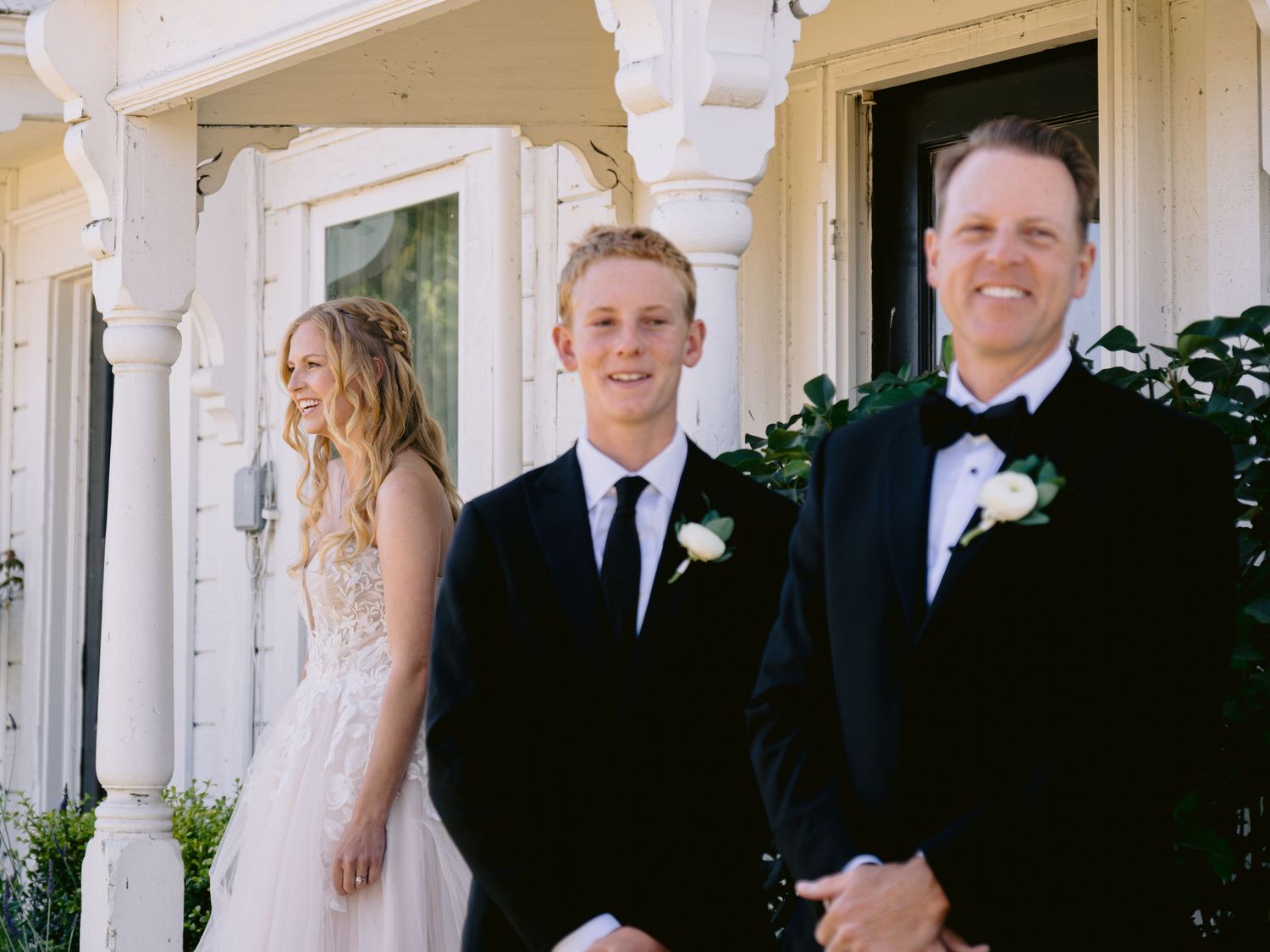 Wedding party members in formal attire stand together in front of a white building.