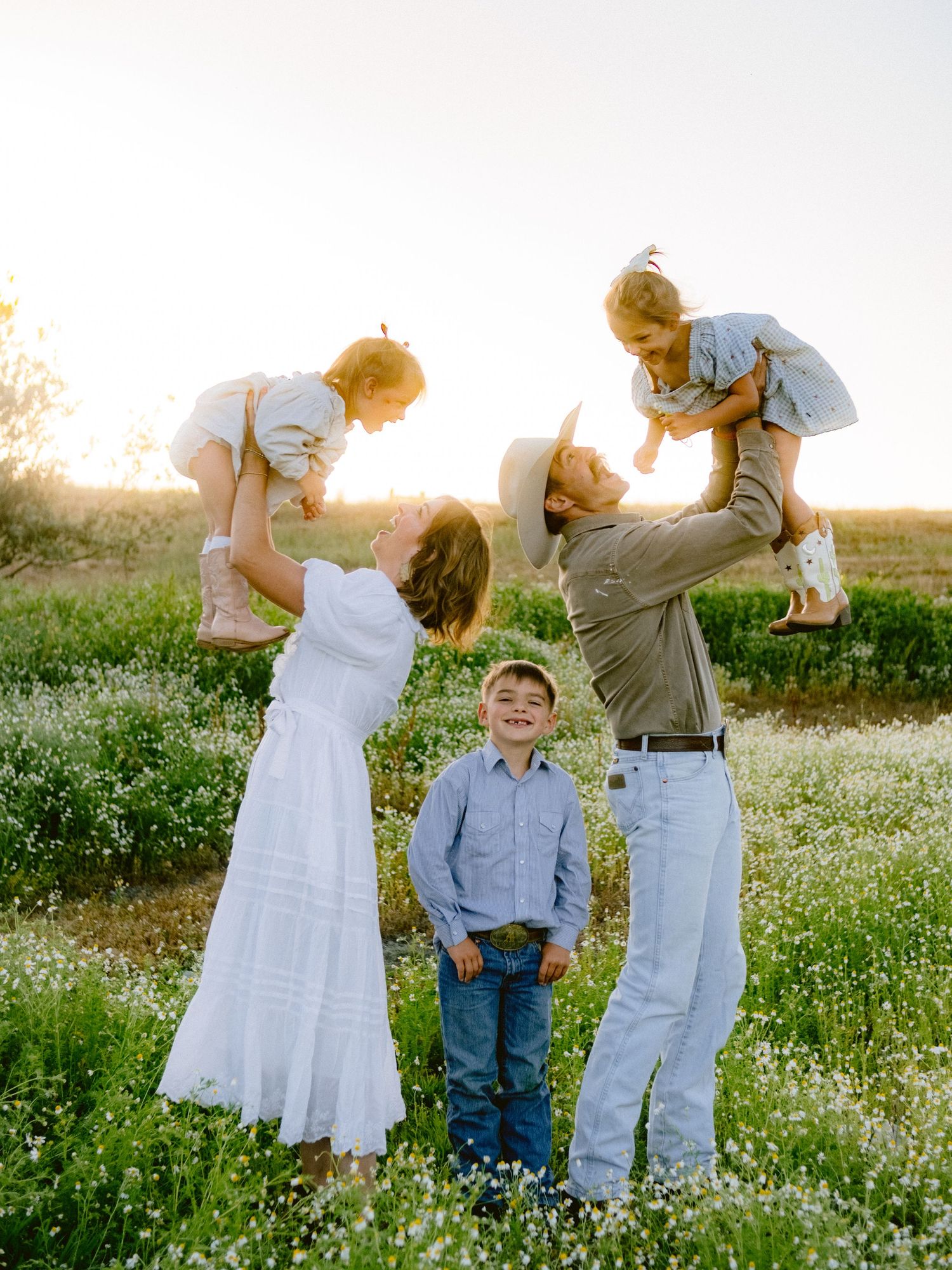 A family plays together in a sunny field of white wildflowers at sunset.
