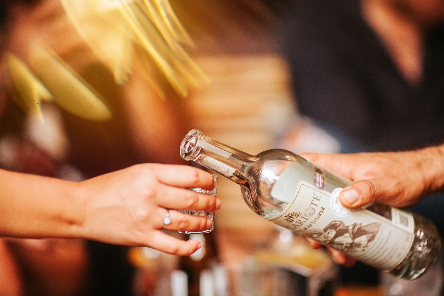 Guests tasting different mezcal options. Ambient lights and festive vibes for an unforgettable celebration.