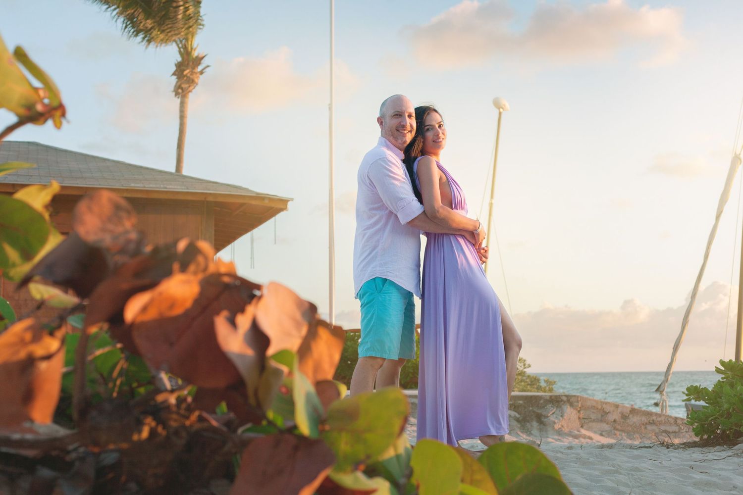 A couple embraces lovingly in the morning light at Bahía Príncipe, surrounded by tropical foliage and a serene beach view.