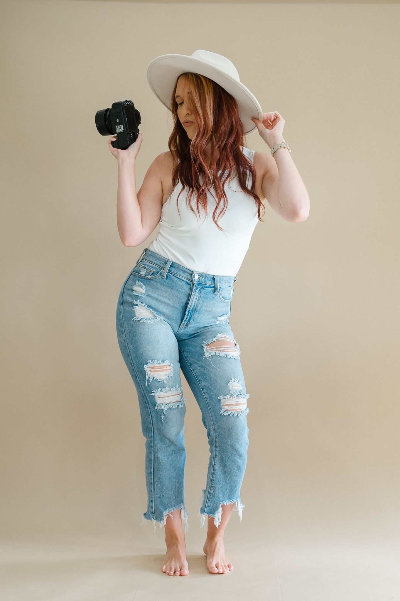Person wearing distressed light blue denim jeans and white top poses in different angles against beige wall.