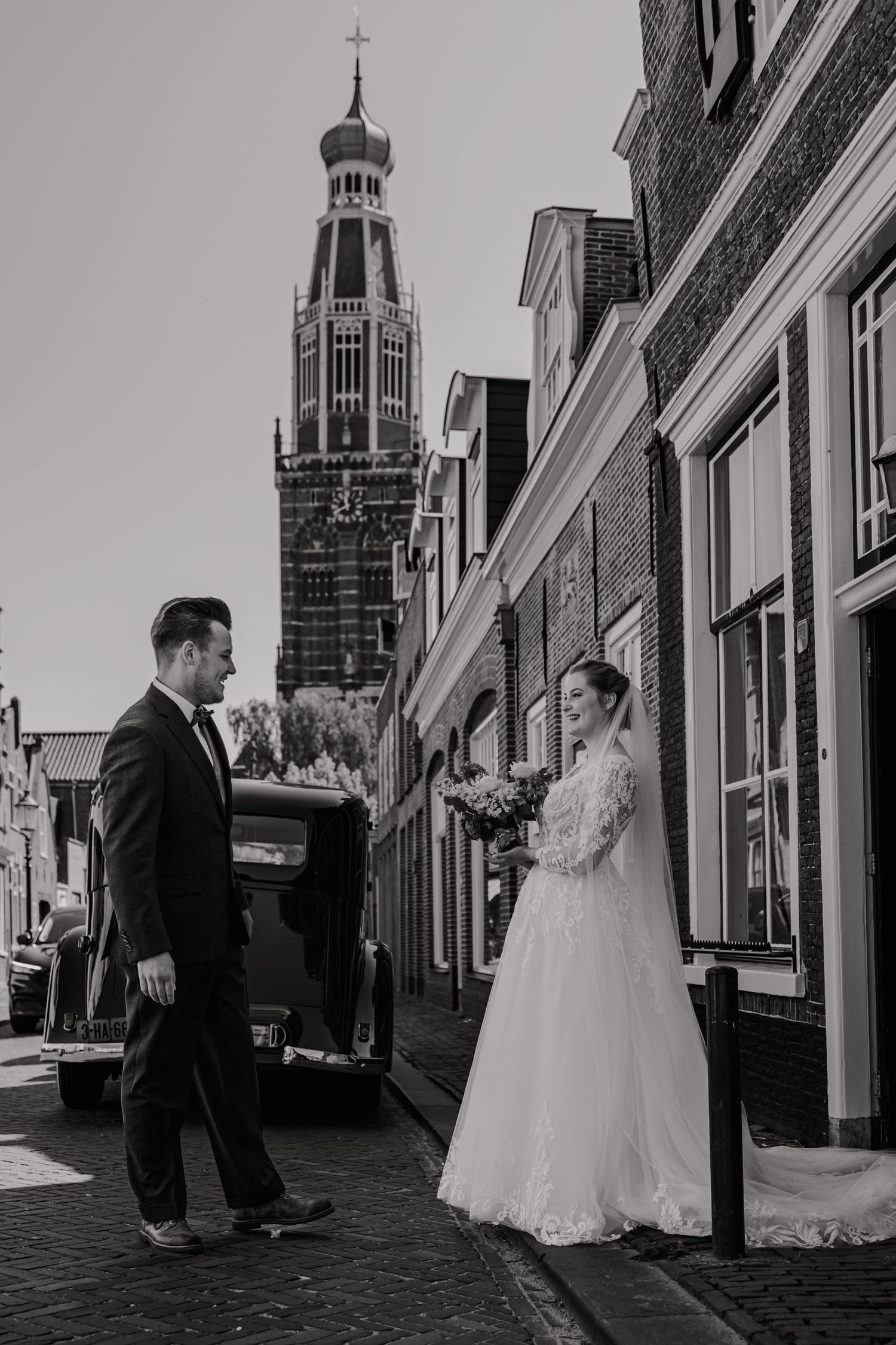 Black and white wedding photo with a church tower in the background on a historic Dutch street.