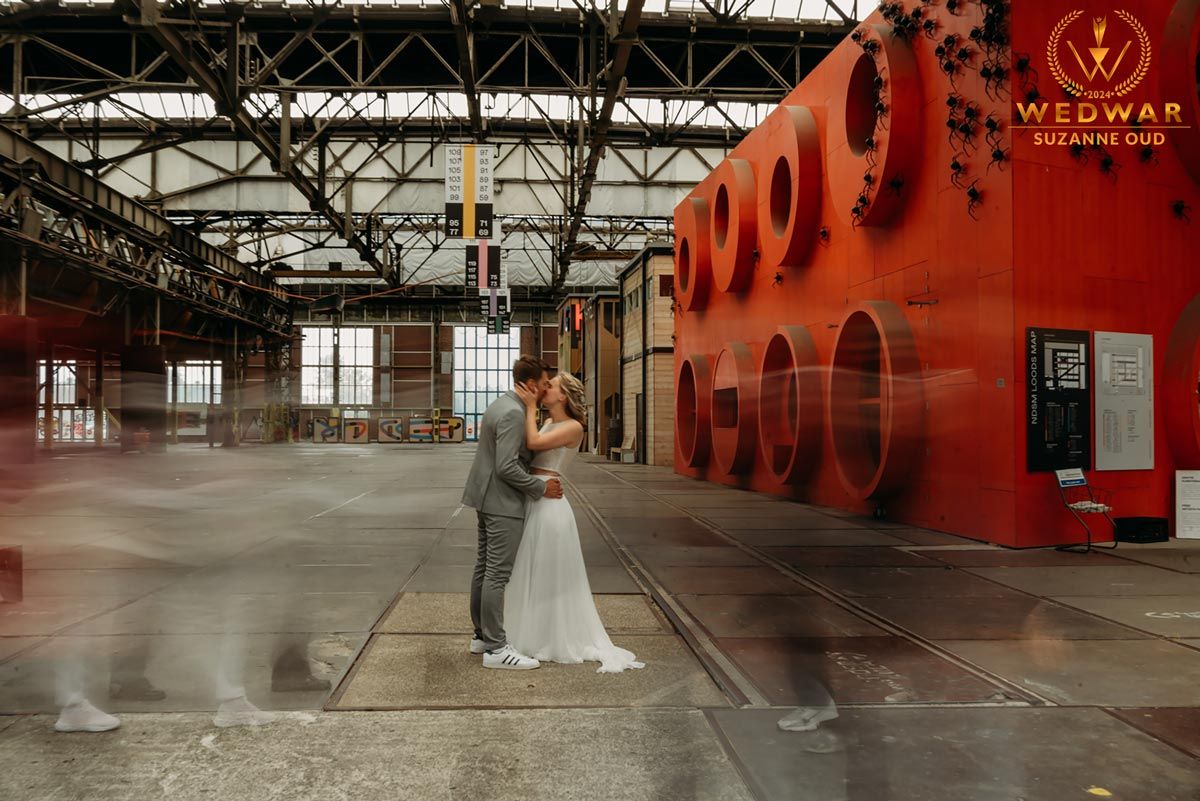 Couple embracing in an industrial warehouse space with bright red wall and geometric patterns.