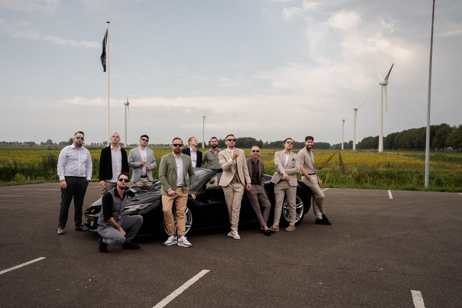 Groomsmen posing with classic cars in parking lot on wedding day.