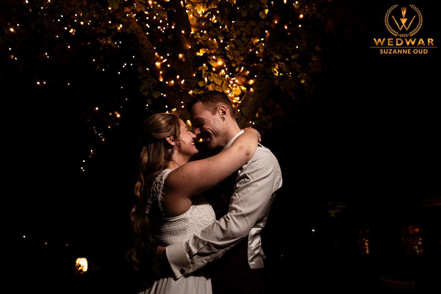 A couple shares a romantic embrace during their wedding celebration with sparkling lights in the background.
