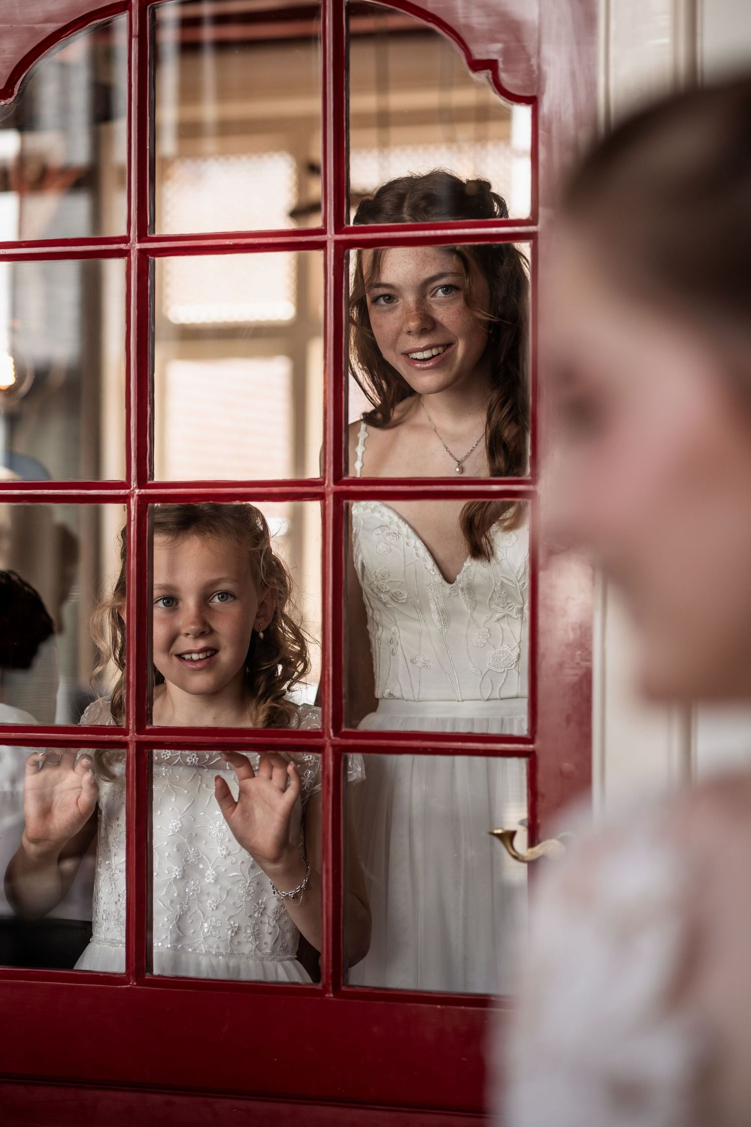 Playful wedding party members peek through red window panes with joyful expressions.