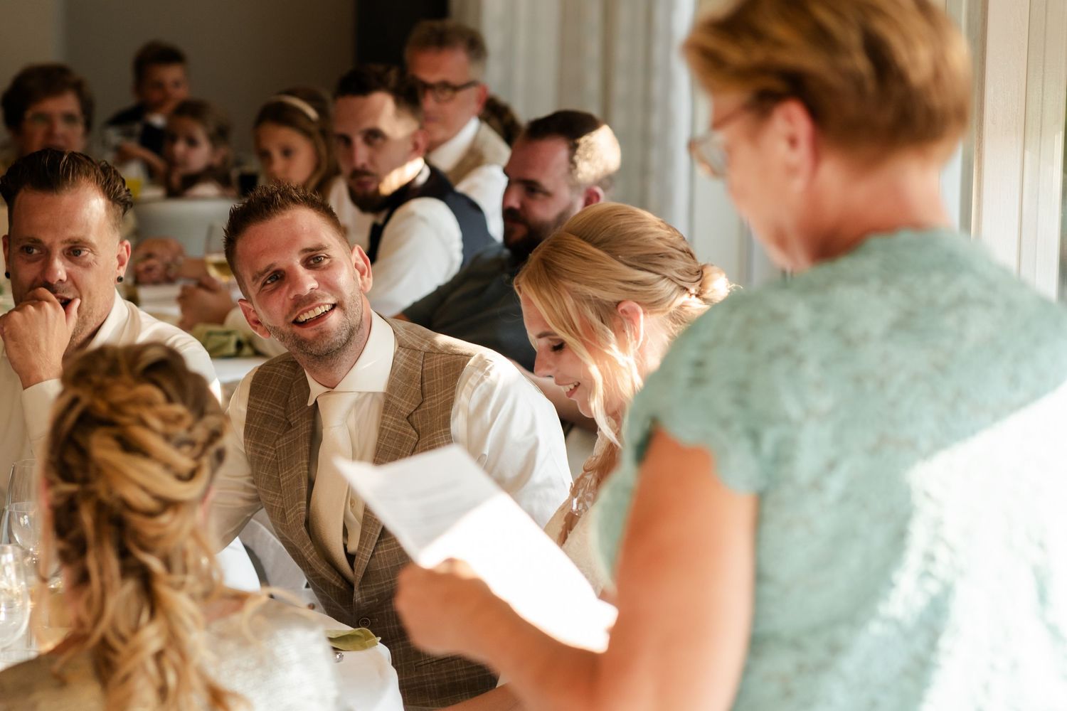 Wedding guests listen attentively during a speech or toast at an indoor reception.