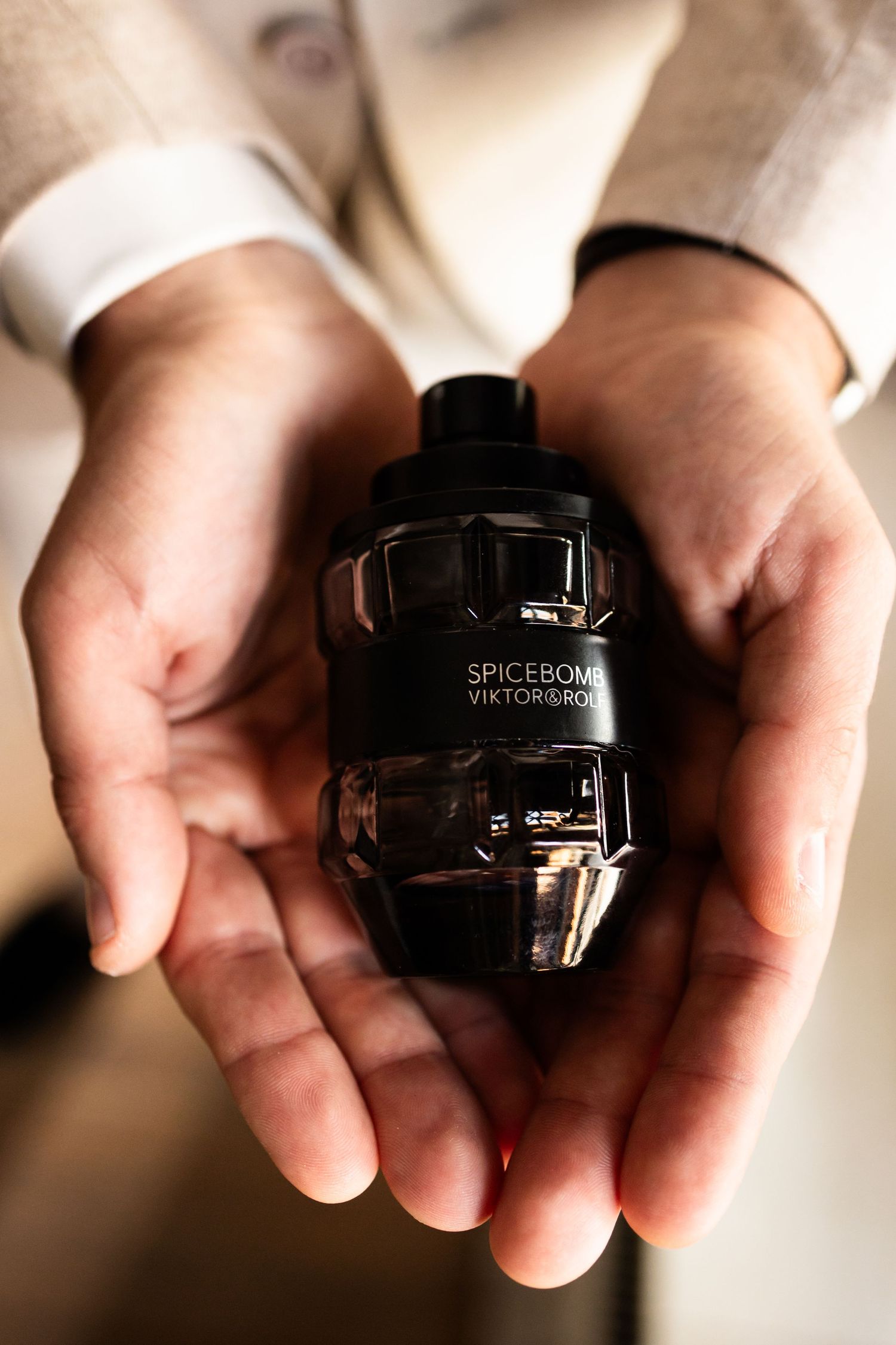 Hands holding a black perfume bottle labeled Spicebomb against a light background.