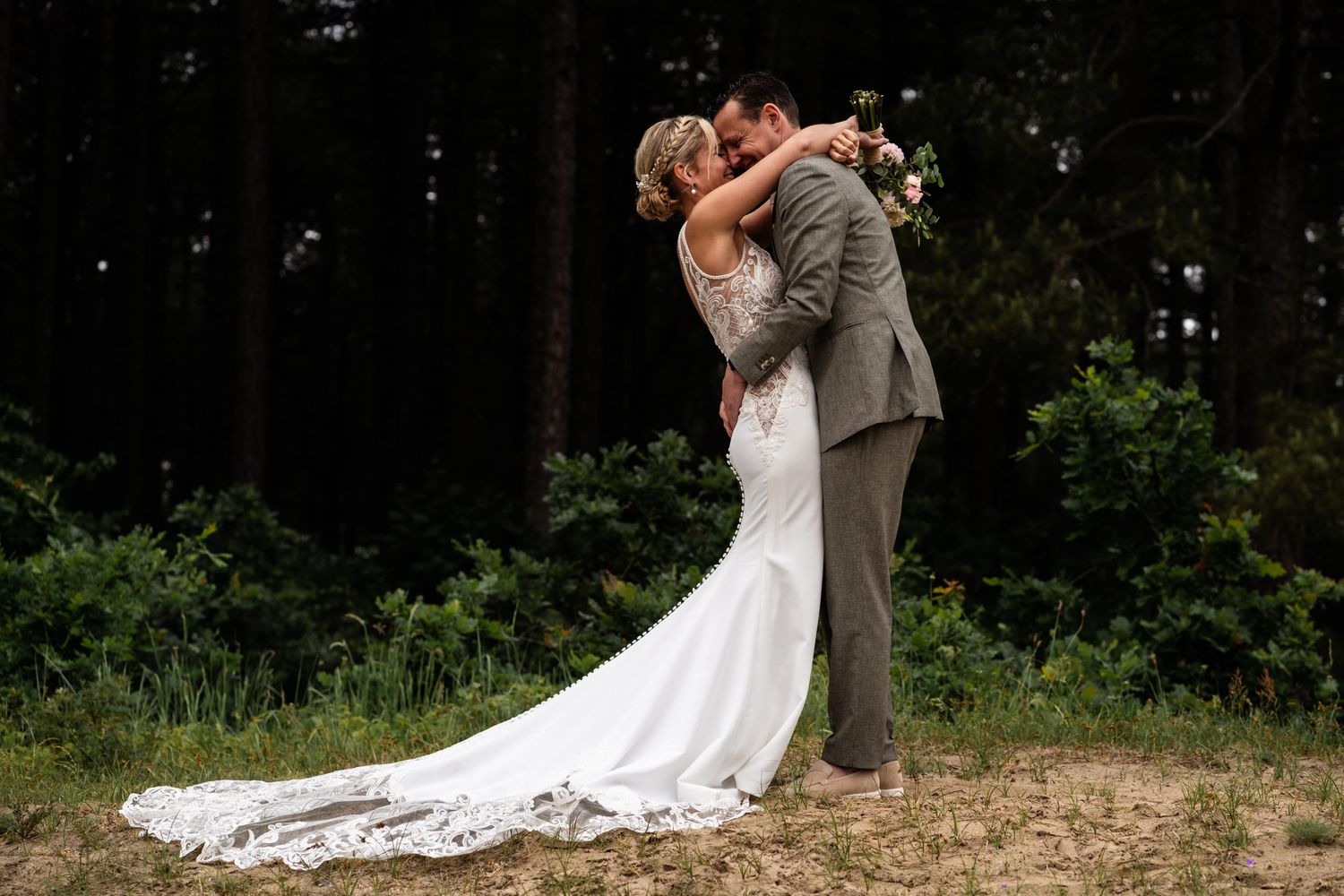 Romantic wedding couple embracing outdoors in a forest setting.