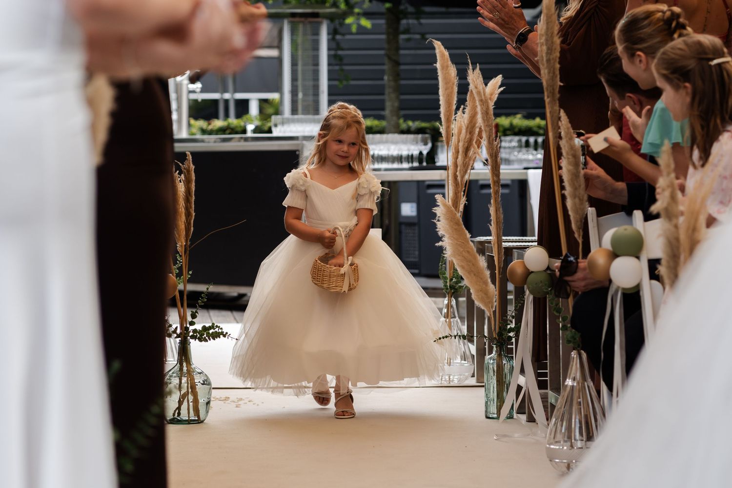 A bride in a flowing white ballgown walks down the aisle at an indoor wedding ceremony.