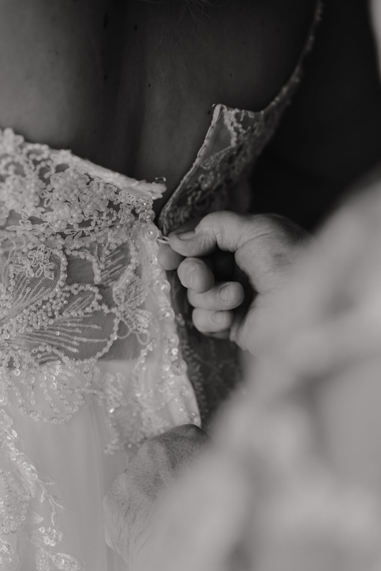 Close-up black and white detail of delicate lace being adjusted on a wedding dress.