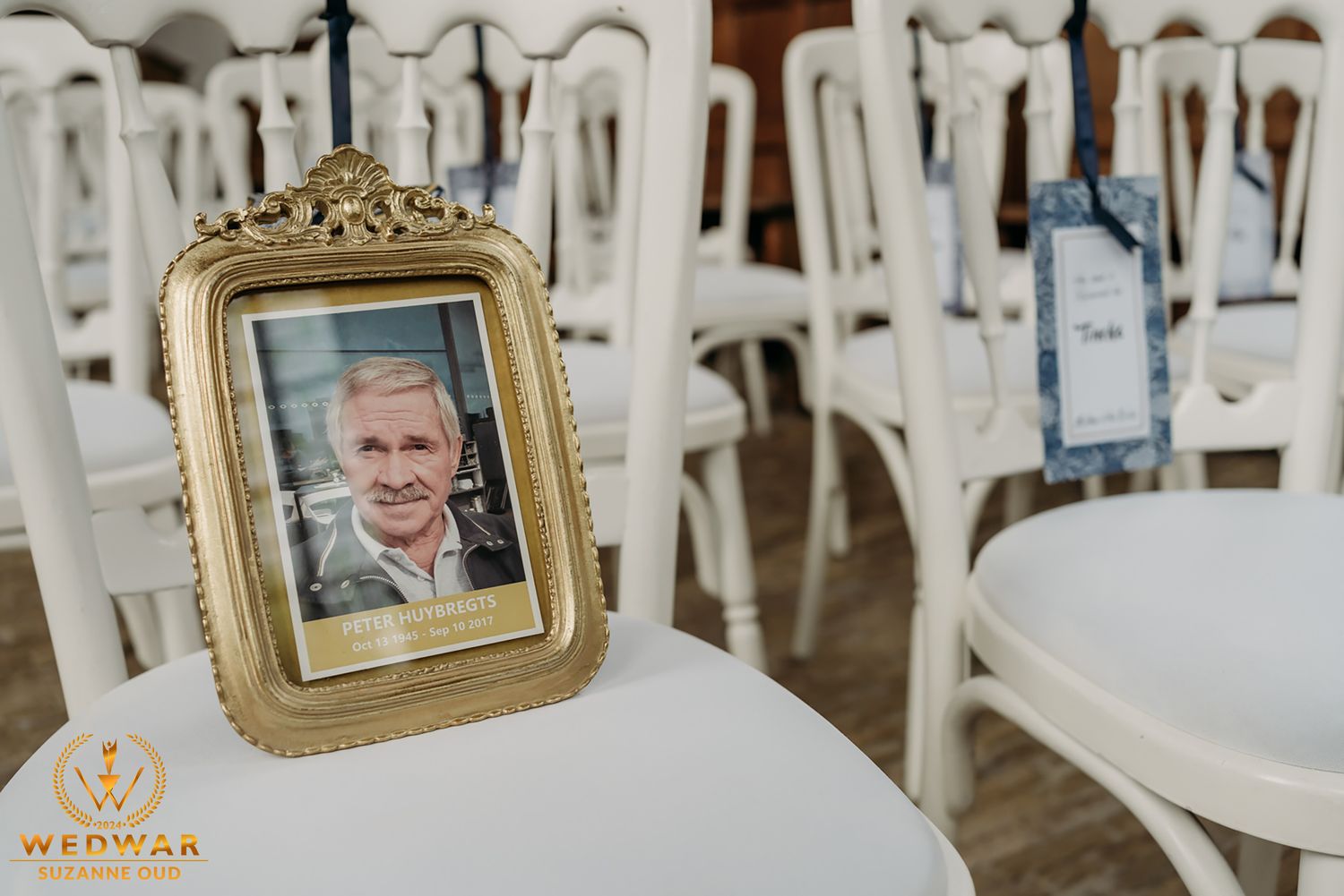 A framed photo on a white chair among rows of empty white chairs at an event setting.