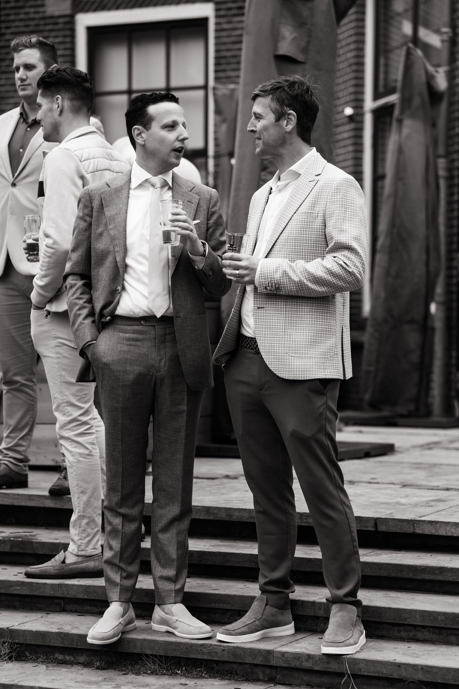 Two well-dressed men having a conversation while standing on stone steps outside a brick building.