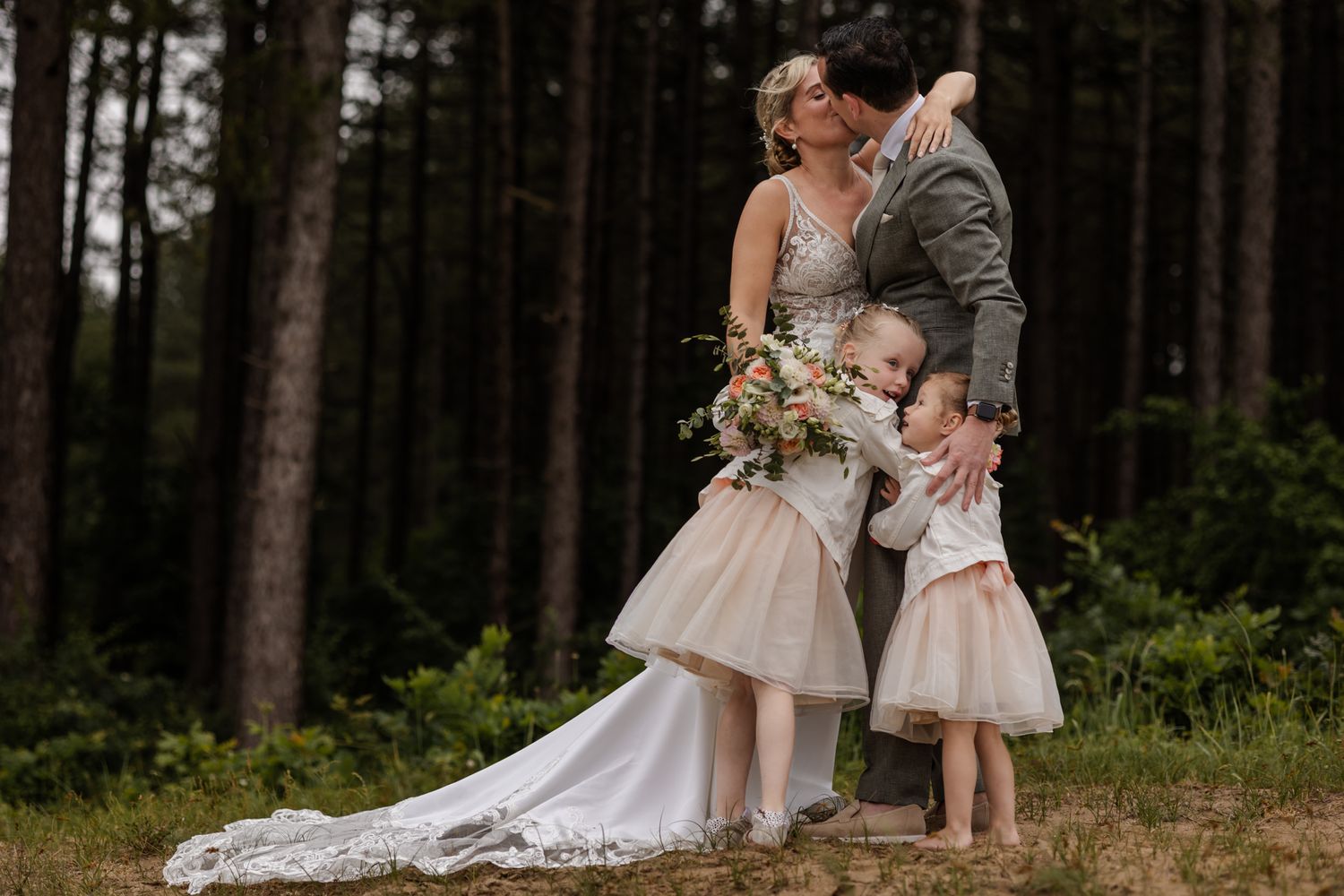 A romantic wedding moment captured in a moody forest setting with two people in formal attire and a young child in pink.