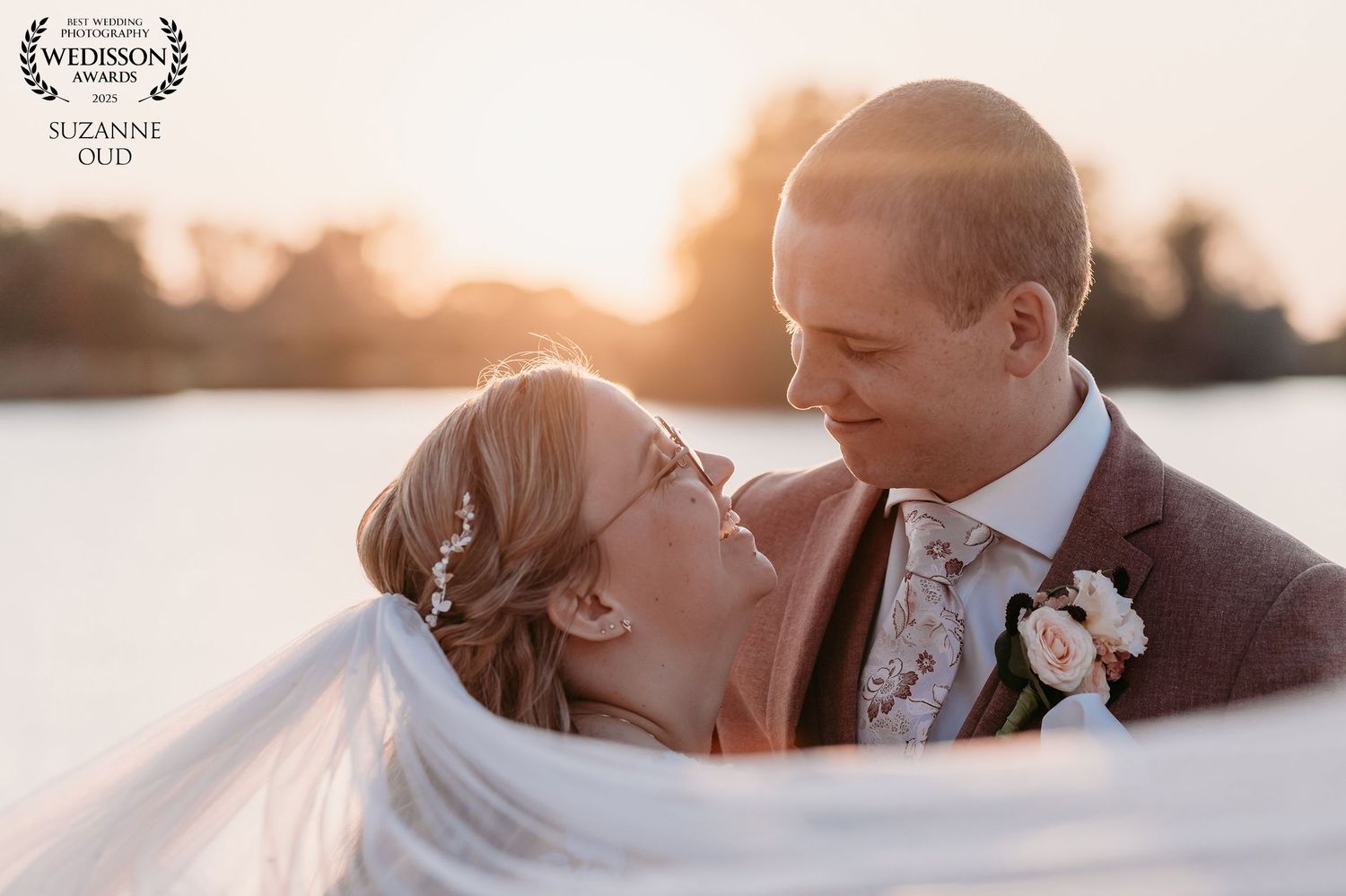 A romantic wedding photoshoot silhouetted against a golden sunset over water creates a dreamy atmosphere.