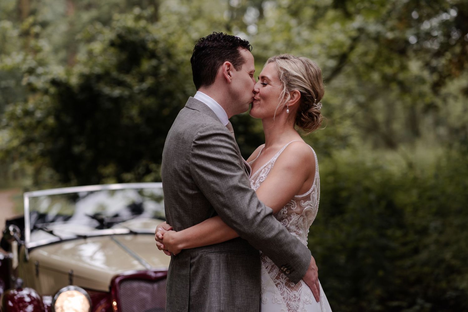 A romantic embrace between newlyweds with a vintage car in the background.