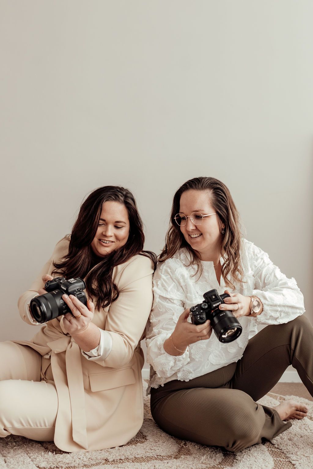 Two women photographers sitting on floor smiling while reviewing photos on their DSLR cameras.