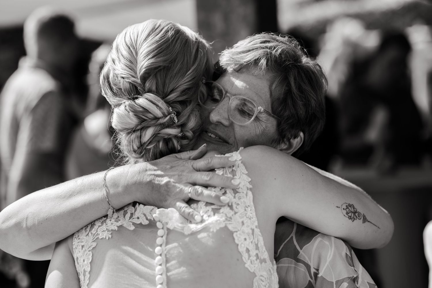 An emotional black and white embrace between two women, one wearing a lace wedding dress, during a special moment.