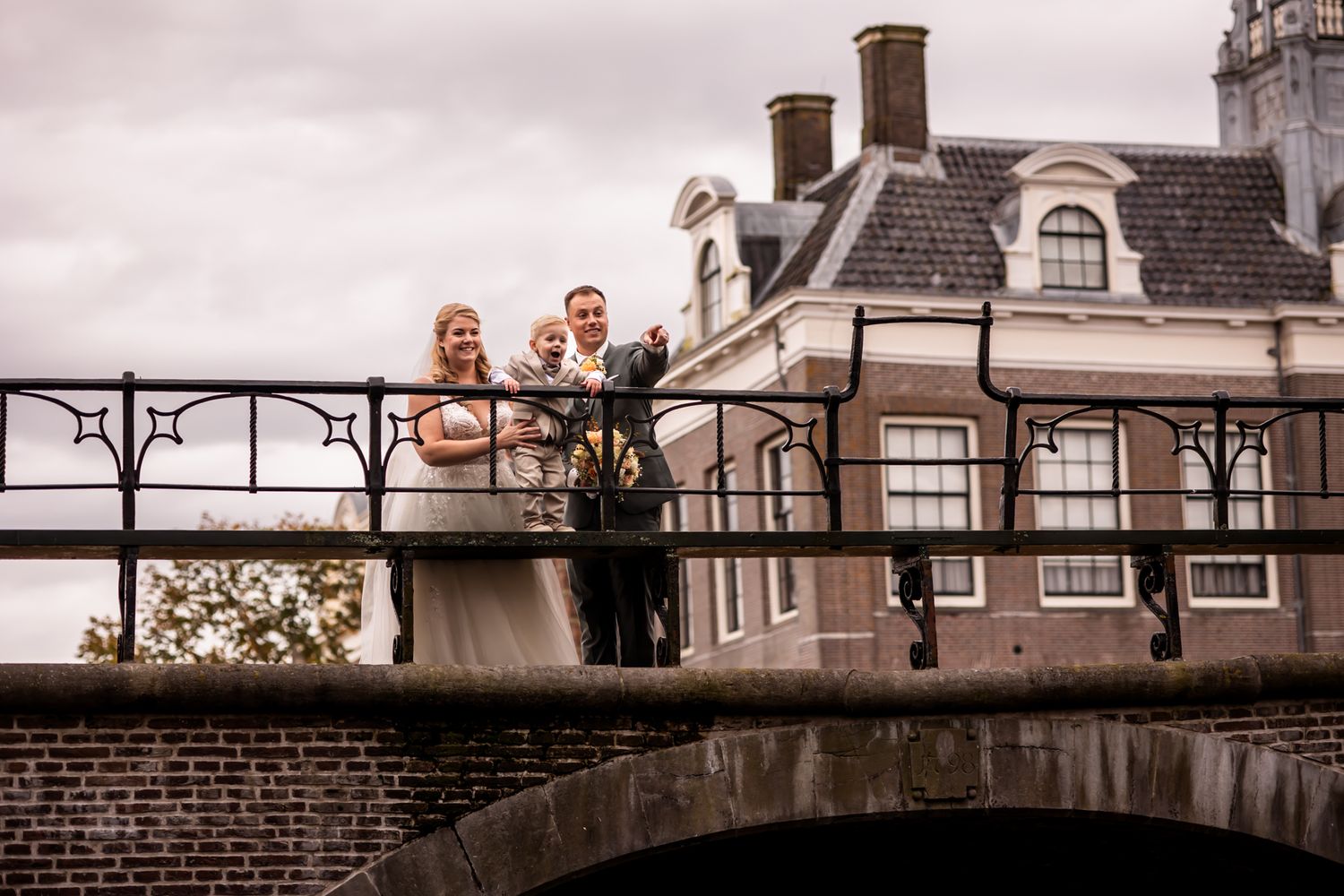 A couple and officiant stand on a historic brick bridge during their Amsterdam wedding ceremony.