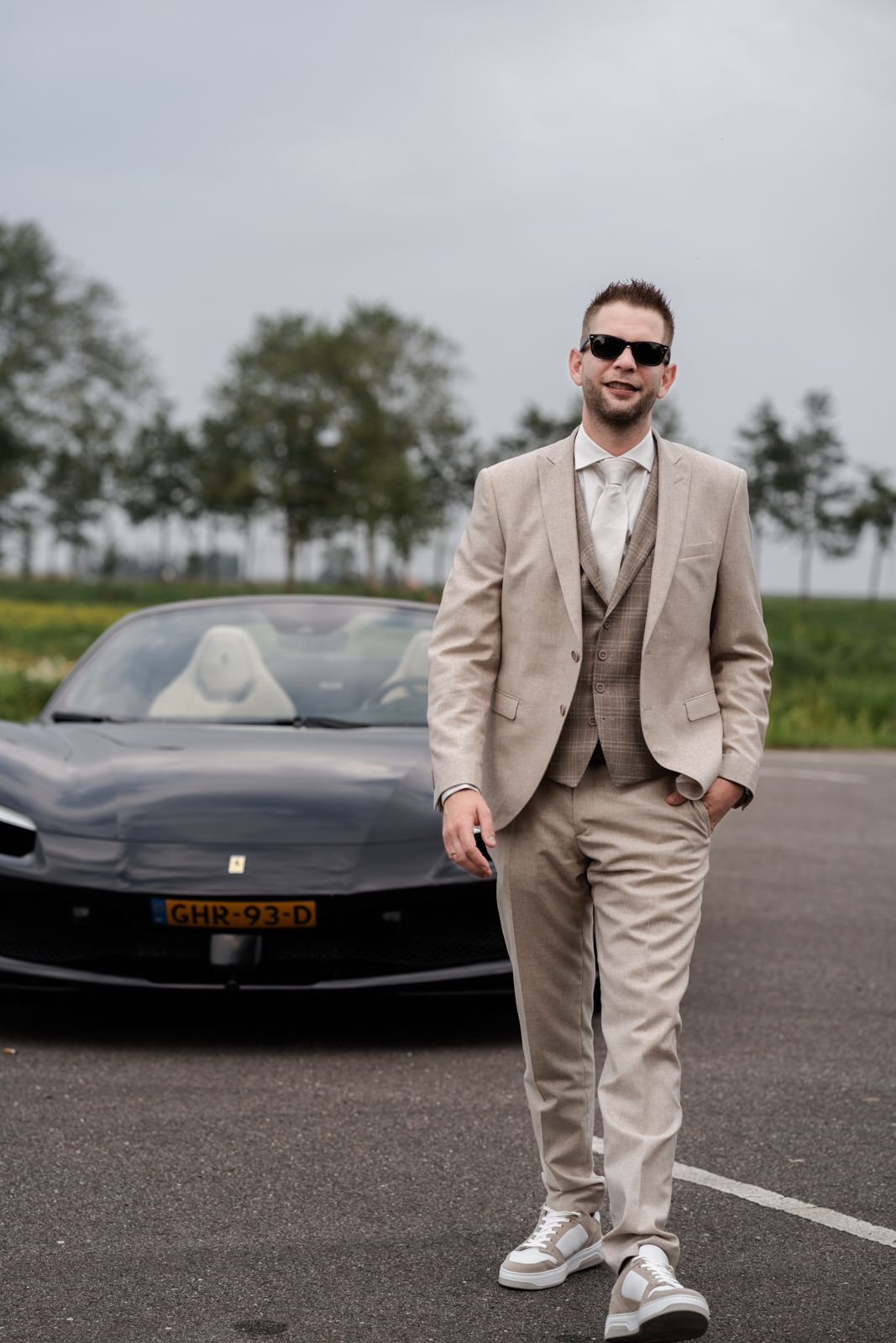 Elegant groom in beige suit poses with luxury sports car.