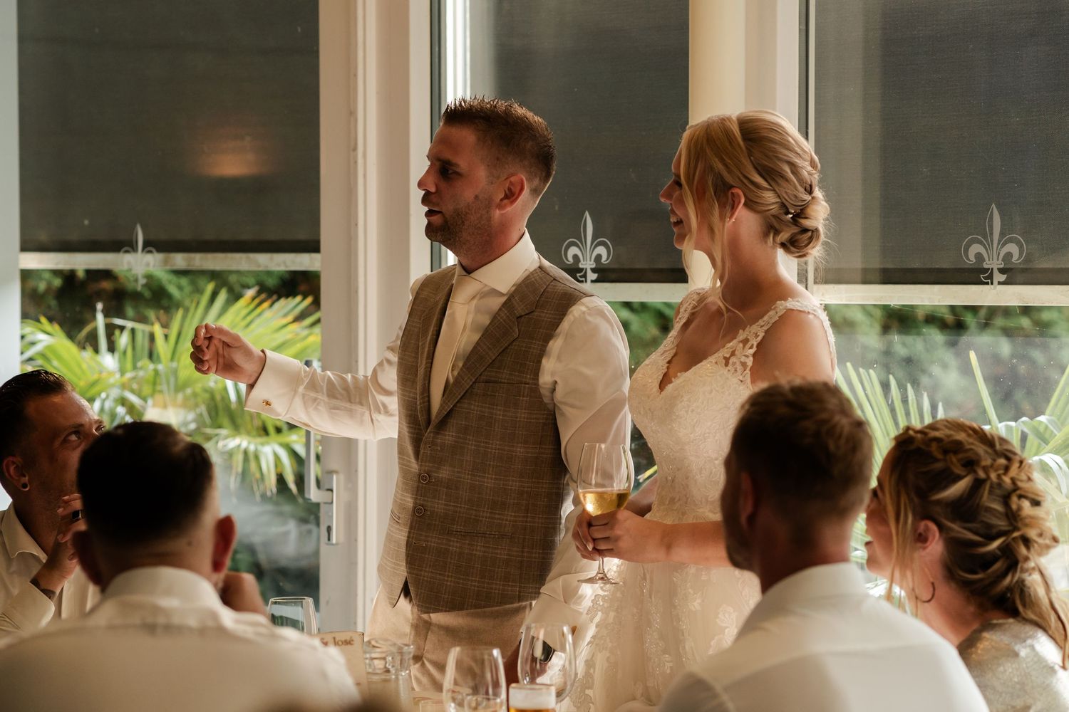 A couple makes a toast at their wedding reception while surrounded by their bridal party seated at the table.