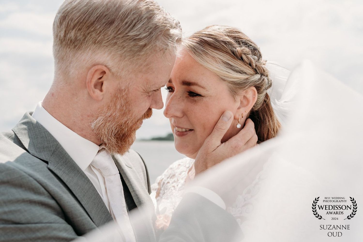 Intimate close-up wedding portrait showing tender moment between couple against bright sky.