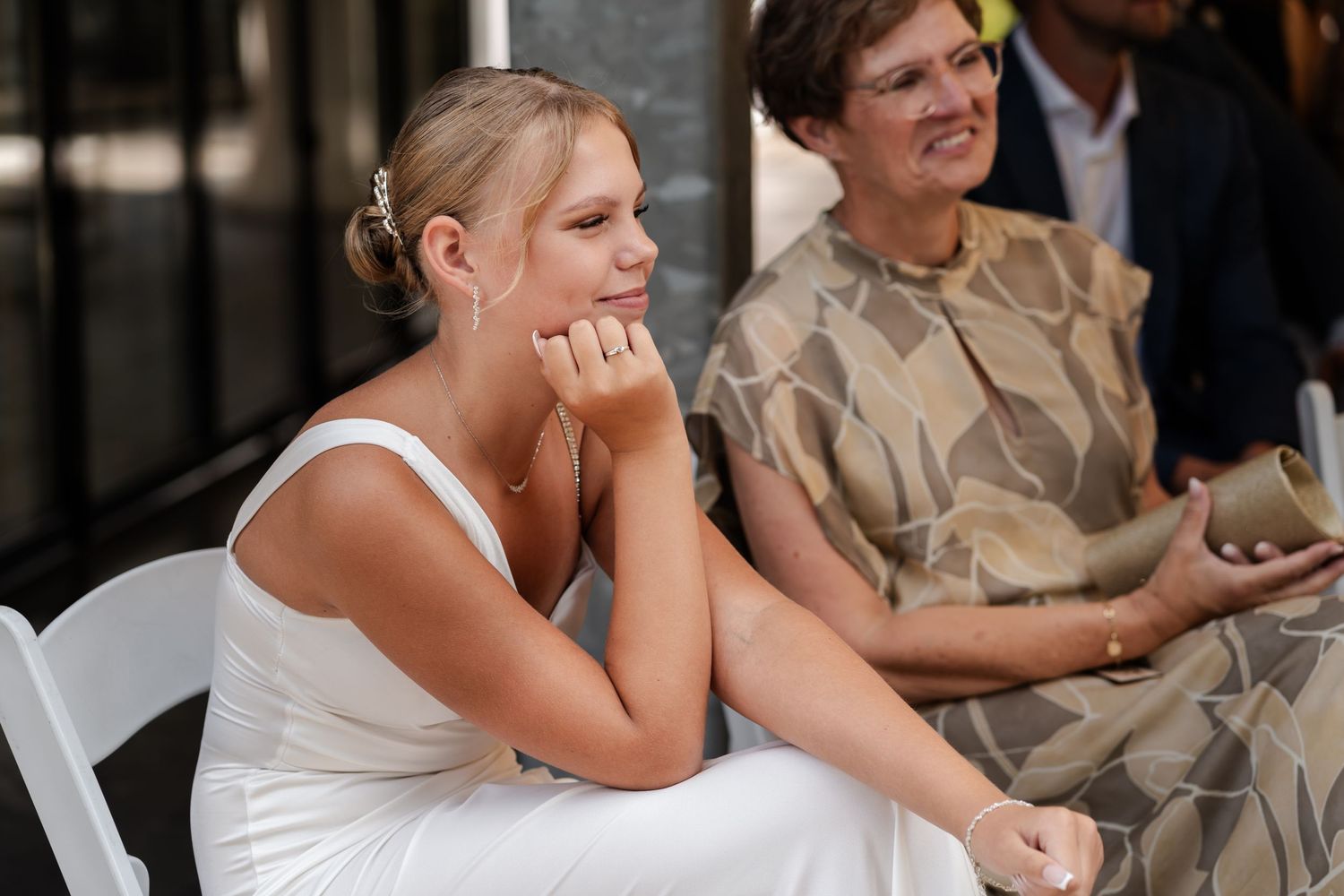 Wedding guests sitting in white chairs at an outdoor ceremony.
