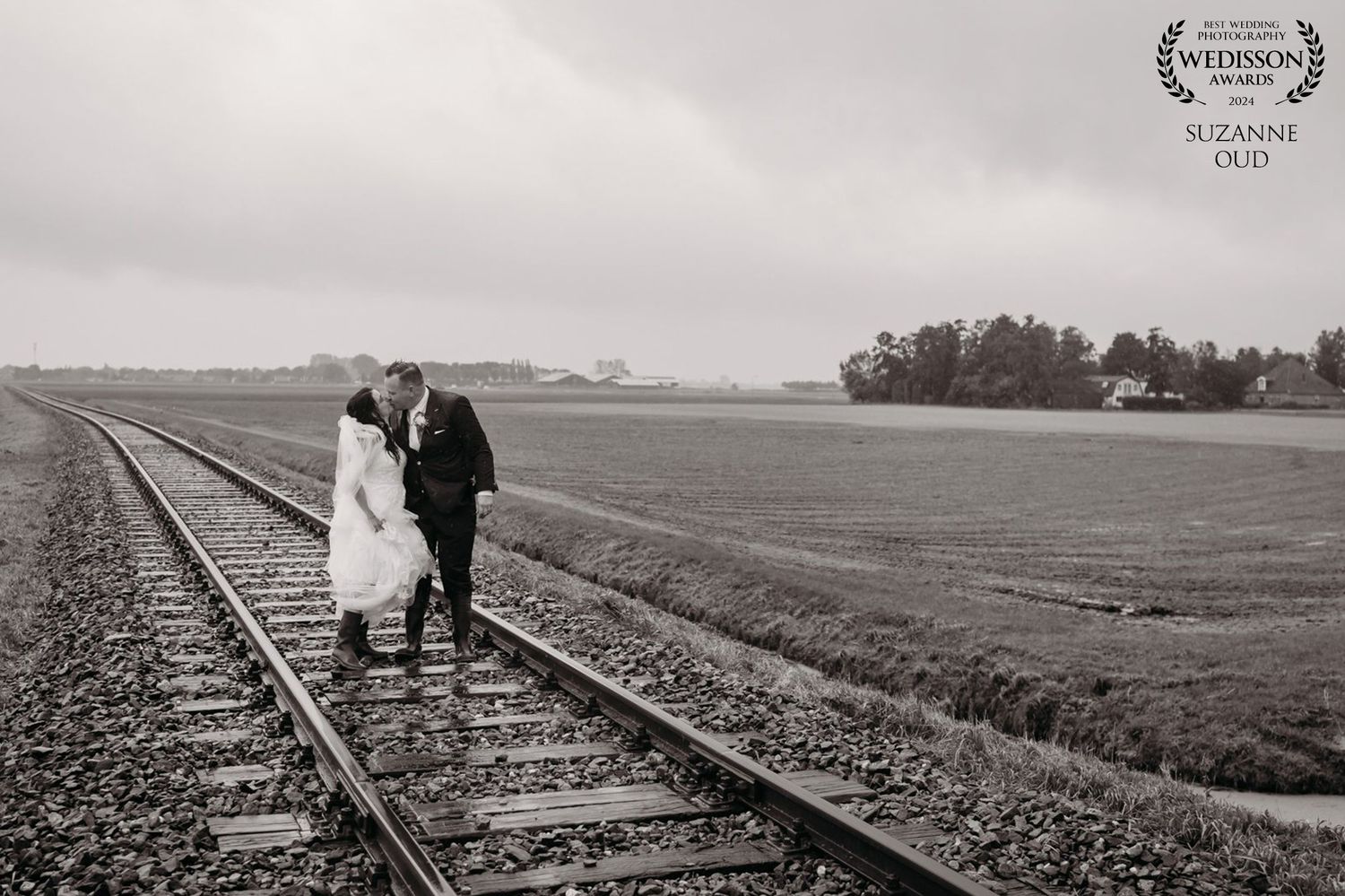 Black and white wedding portrait of couple standing on railroad tracks in rural setting.