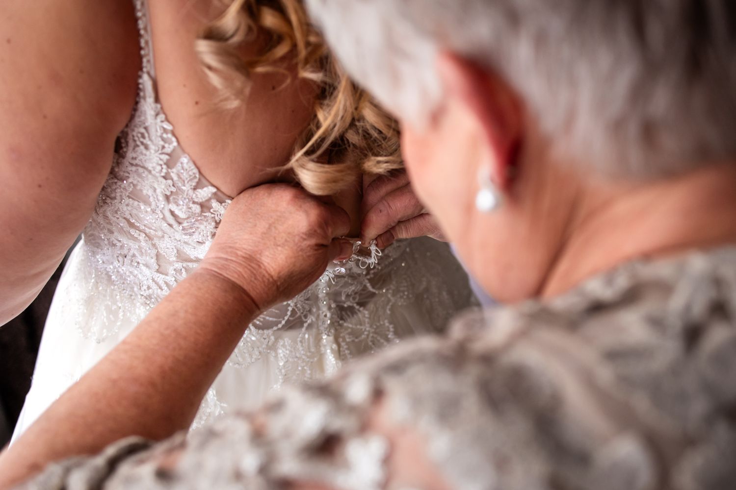 Close-up of delicate lace wedding dress being fastened with intricate beading detail.