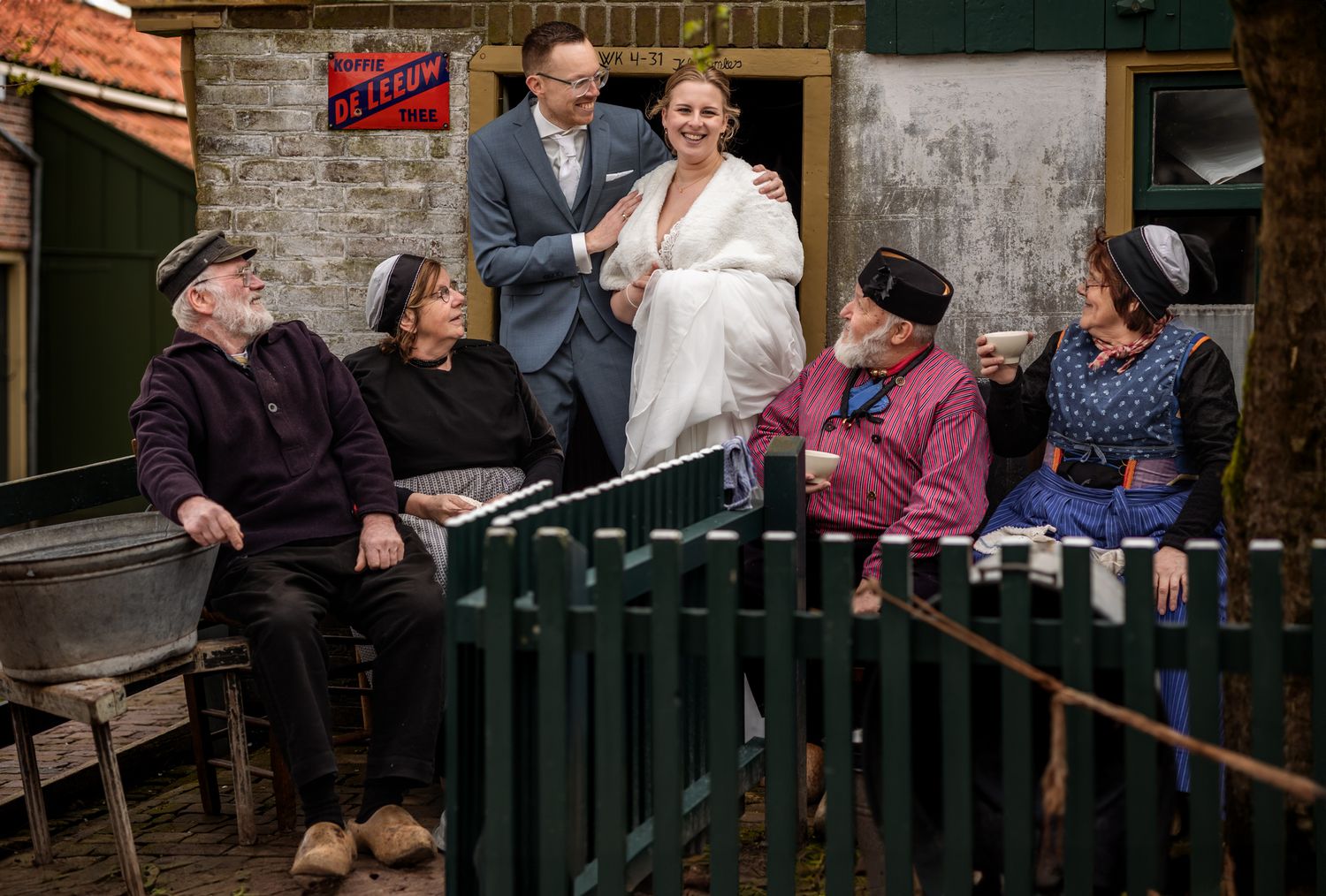 Wedding party gathered on rustic bench outside vintage building.