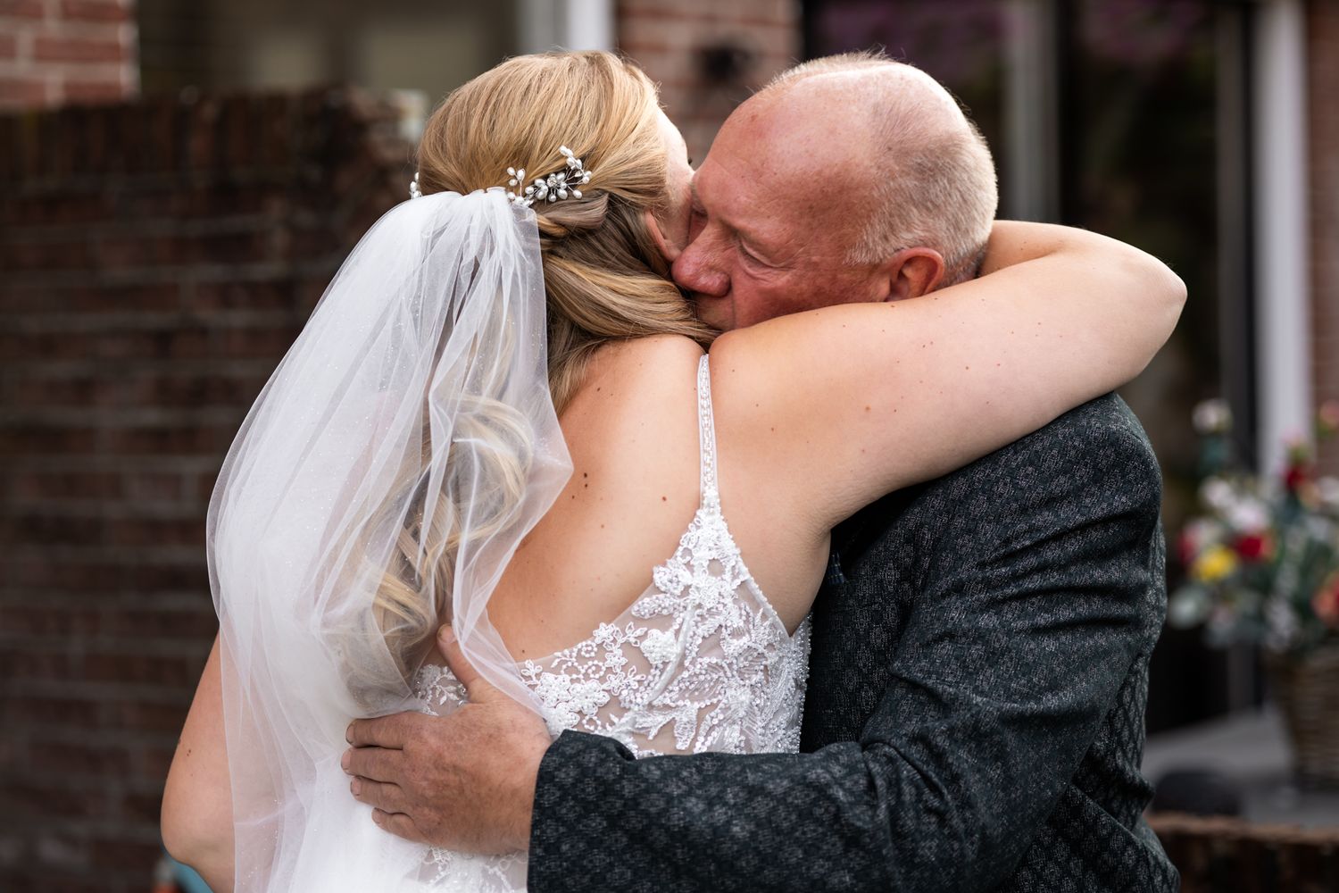 Emotional moment as father embraces bride in lace dress during outdoor wedding ceremony.