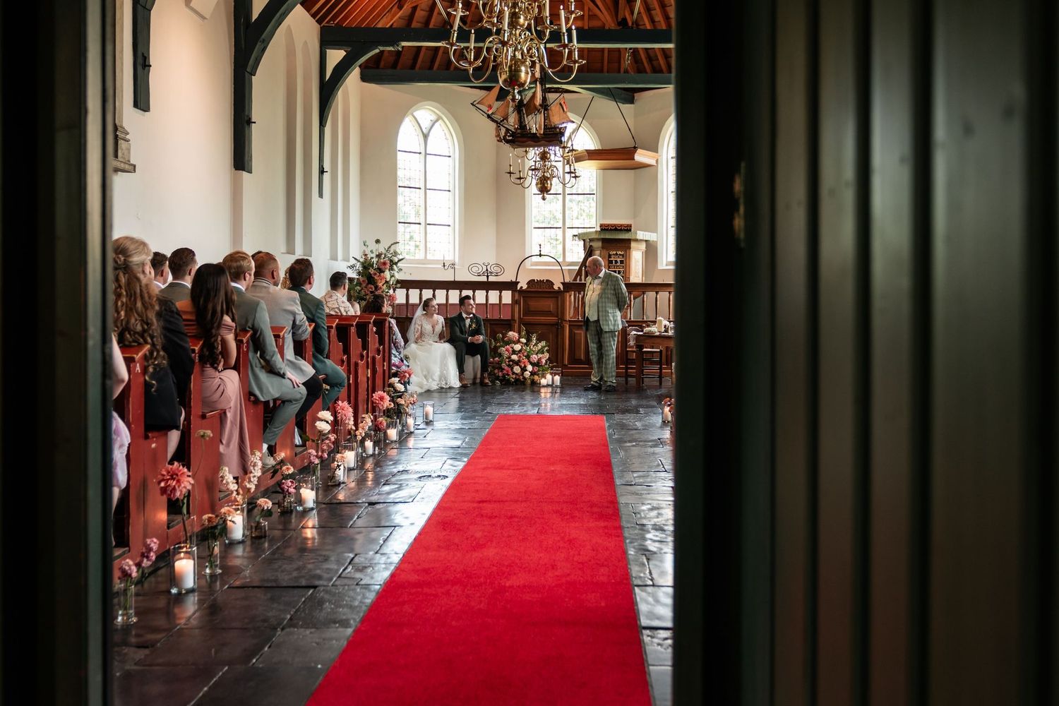 A long red carpet leads down the aisle of a historic church interior with guests seated on both sides.