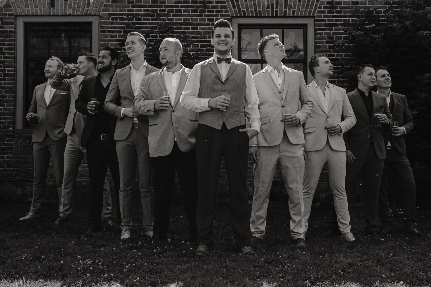Black and white photograph of groomsmen in formal attire standing in a line outdoors.