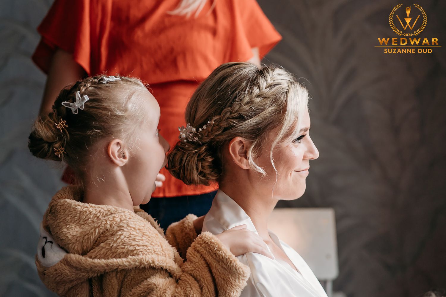 Two people wearing braided hairstyles sitting together during wedding preparations.