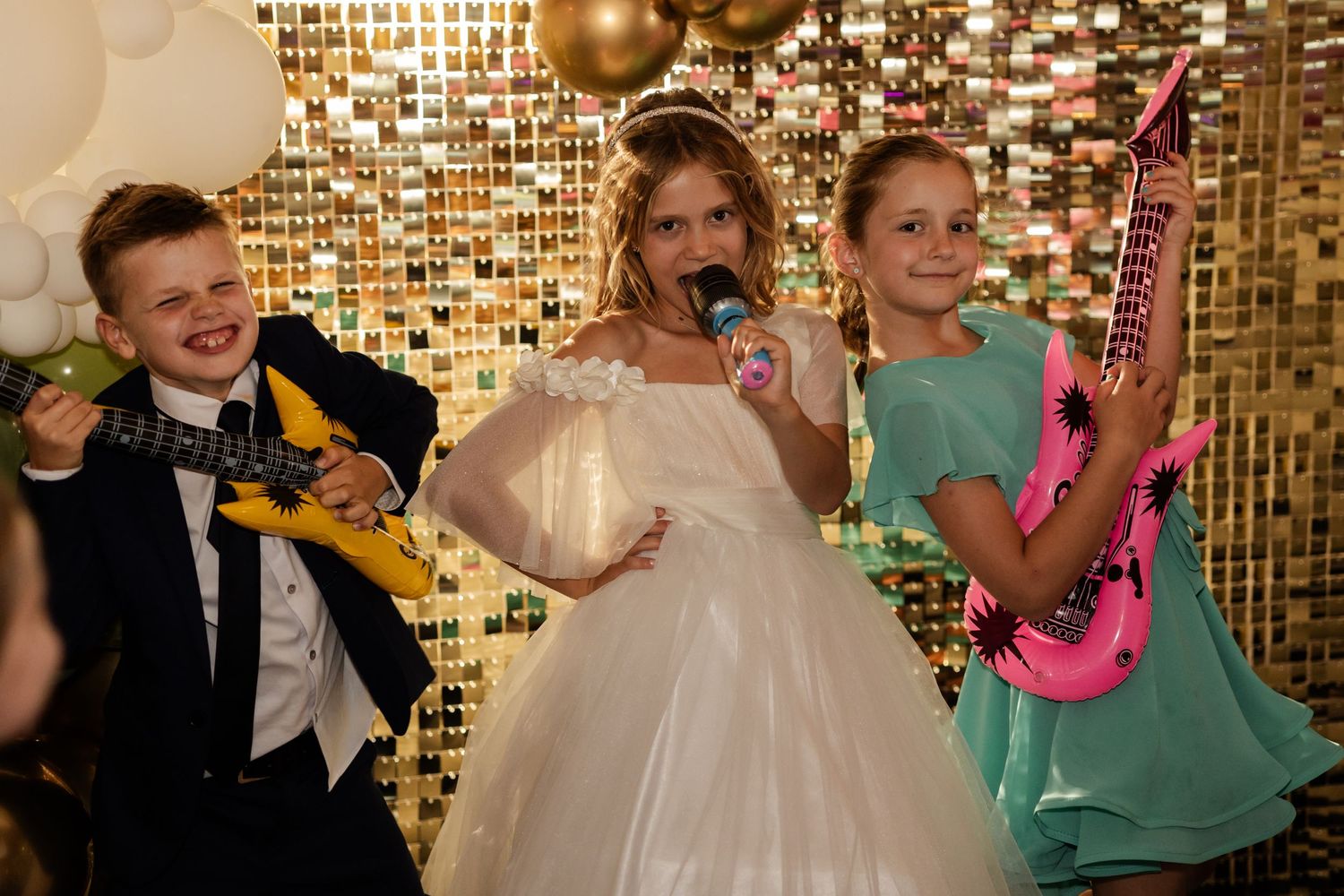 People pose with colorful prop guitars against a gold sequin backdrop at a wedding celebration.