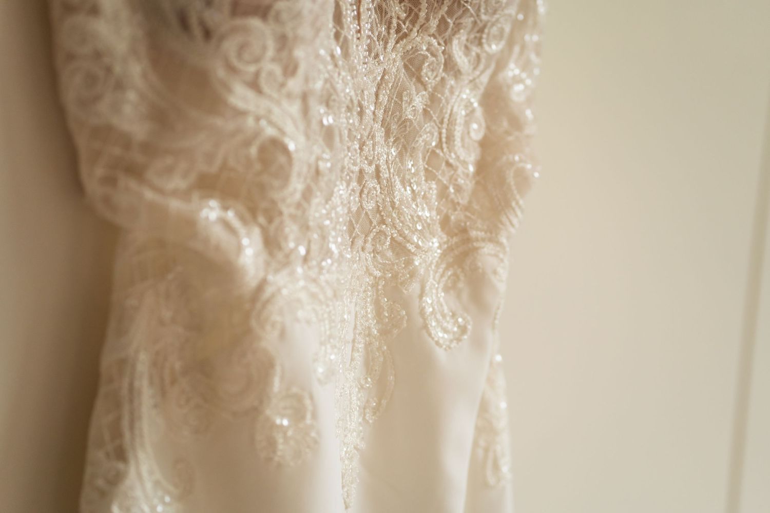 Close-up detail of delicate lace embroidery on a white or cream colored wedding dress hanging.