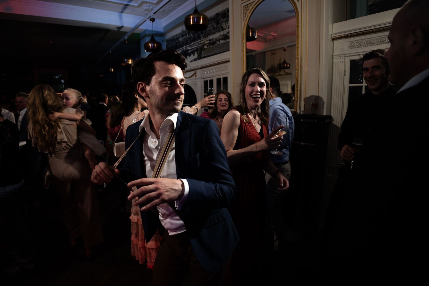 Wedding reception guests dancing and celebrating in dimly lit indoor venue.