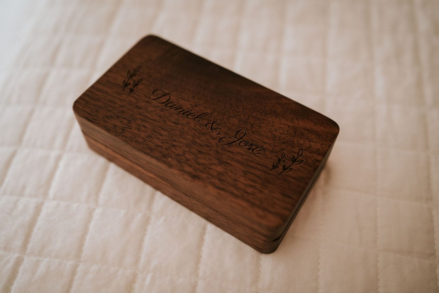 A wooden box with engraved text sits on a white textured surface in soft natural lighting.