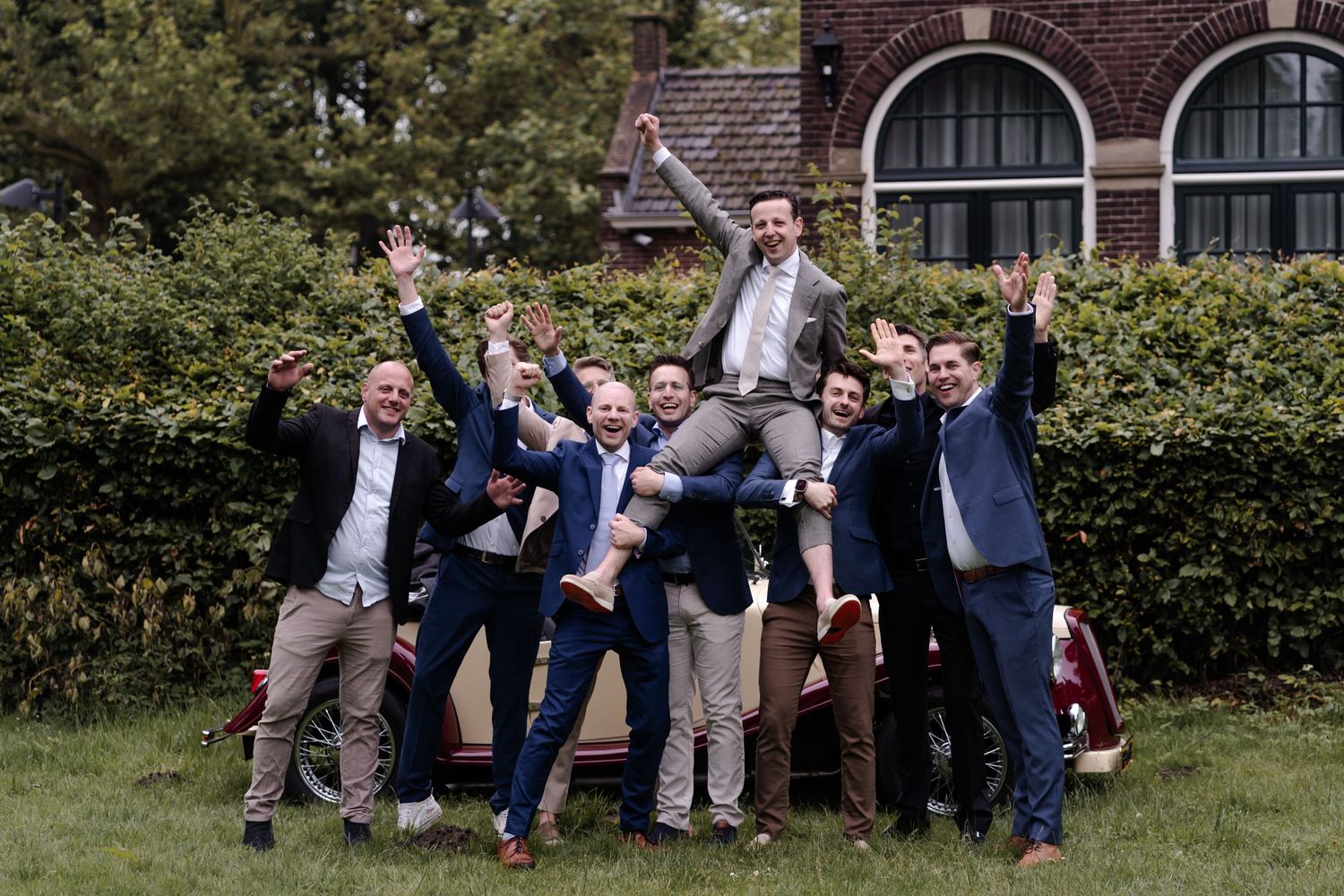 A fun group photo of groomsmen lifting and celebrating in a garden setting.