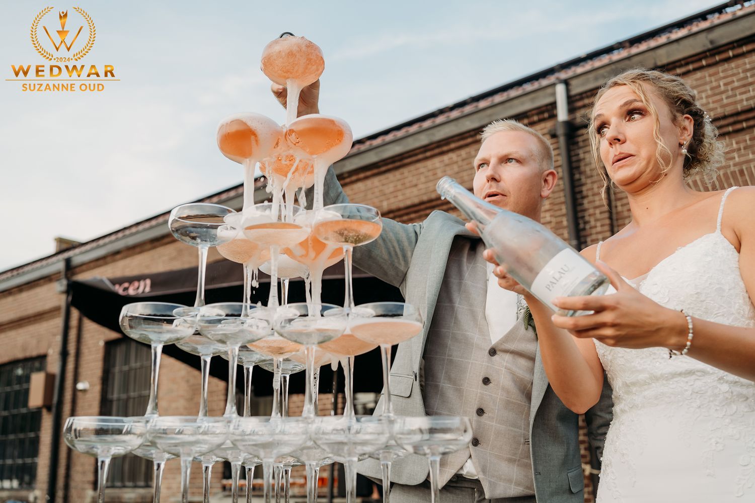Couple pouring champagne into a tower of glasses at their wedding reception.