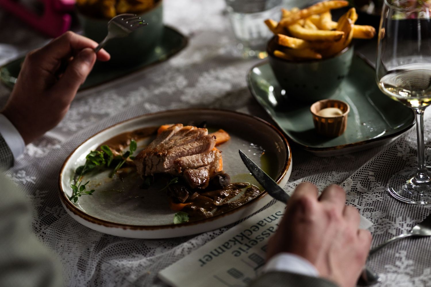 Elegant plated dinner with meat and sides served on formal place settings with ambient lighting.