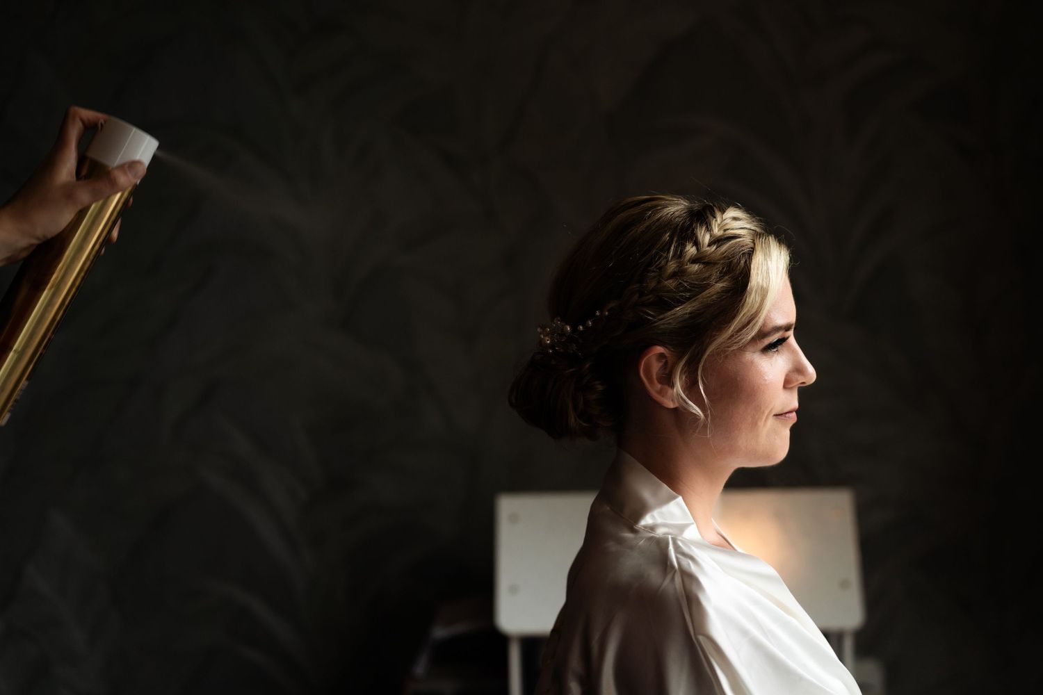 Side profile of a person with an elegant updo hairstyle and white shirt against a dark moody background.