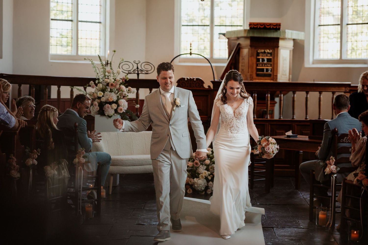 Bride and groom walking down the aisle together in a charming white chapel, smiling joyfully after their wedding ceremony.