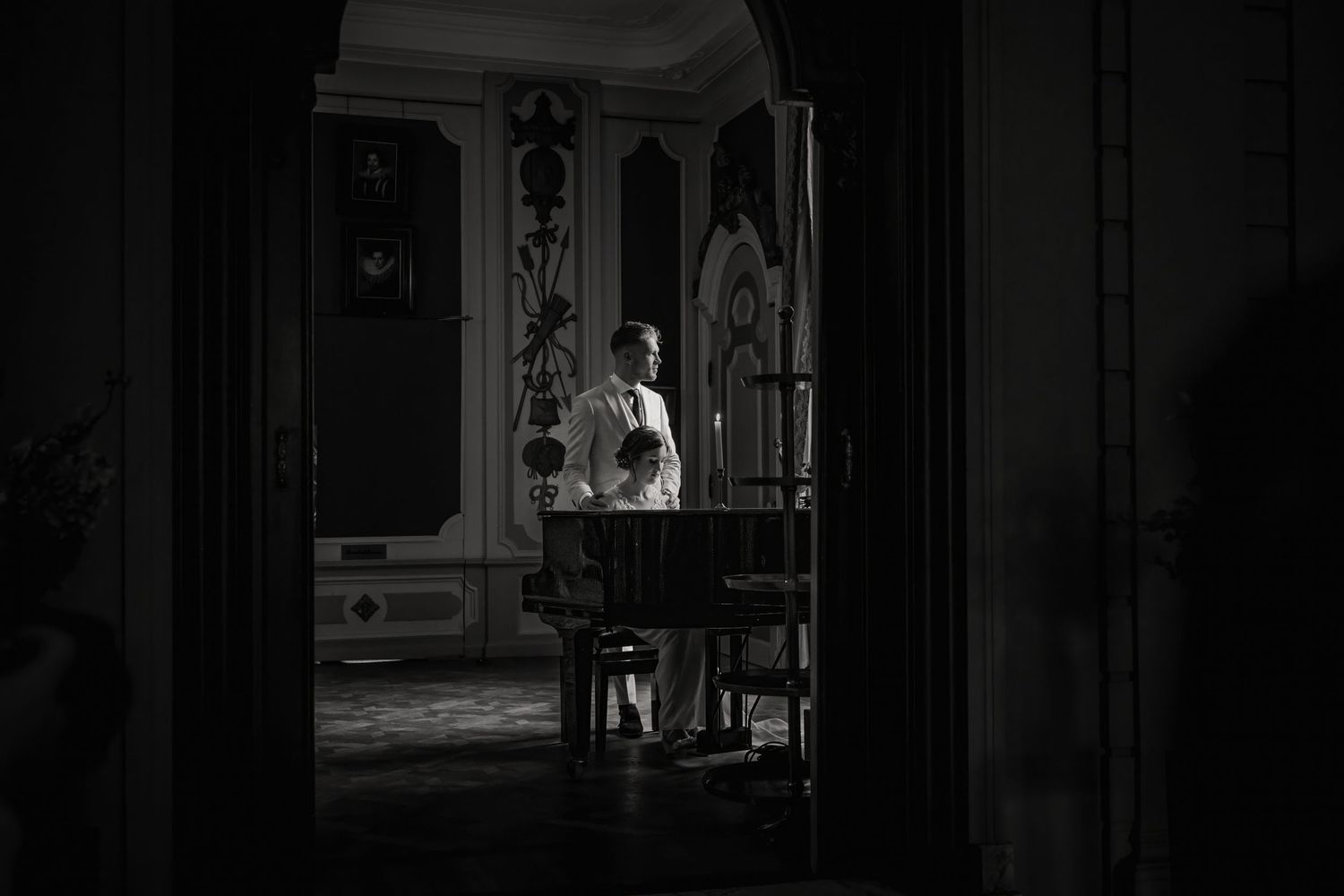 A dark and moody black and white film noir scene showing figures in a dimly lit corridor.