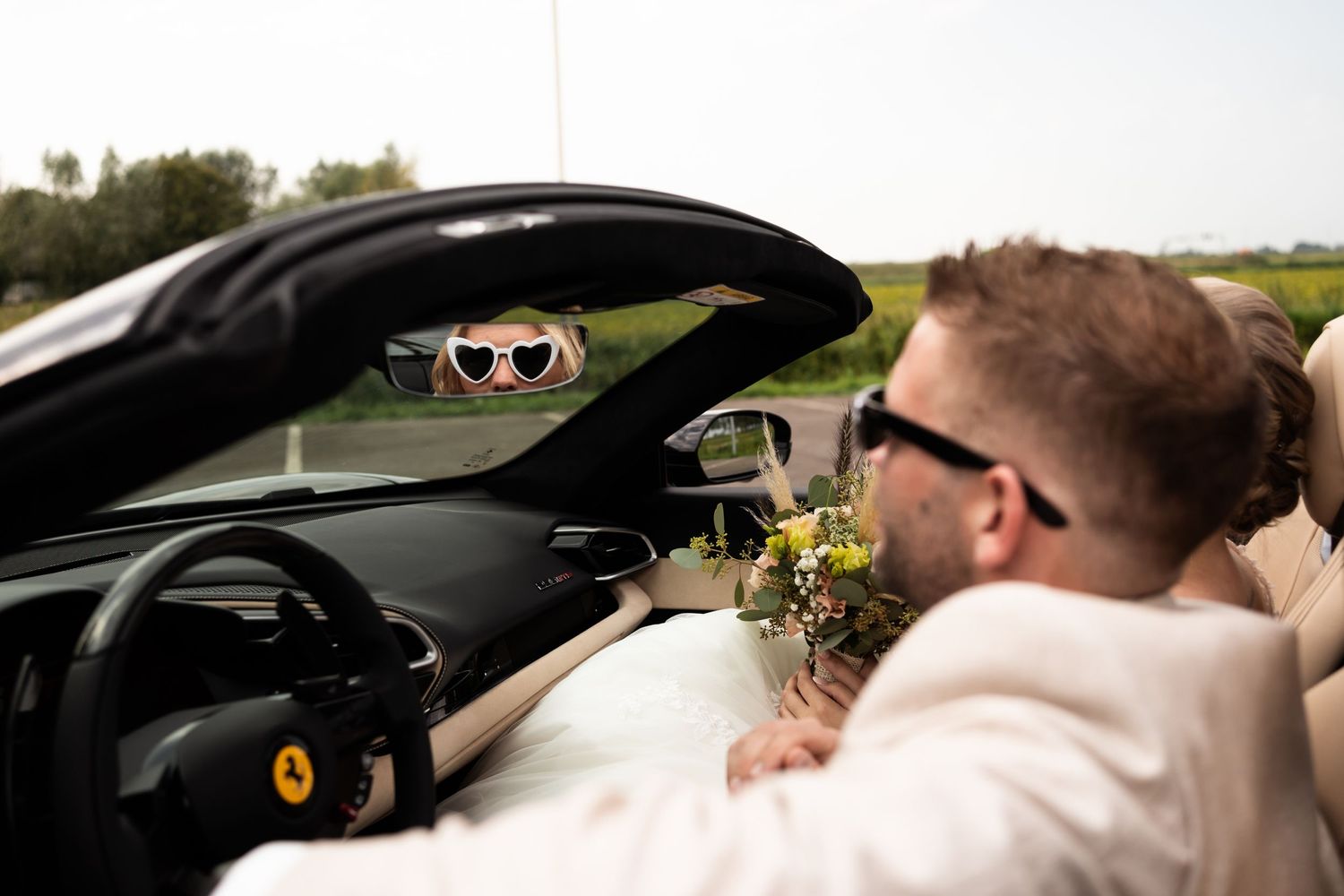 View through a black sports car window showing wedding day celebrations.